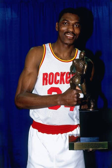 身穿火箭隊球衣的籃球運動員在藍色窗簾前手持獎盃。 — NBA 壁紙