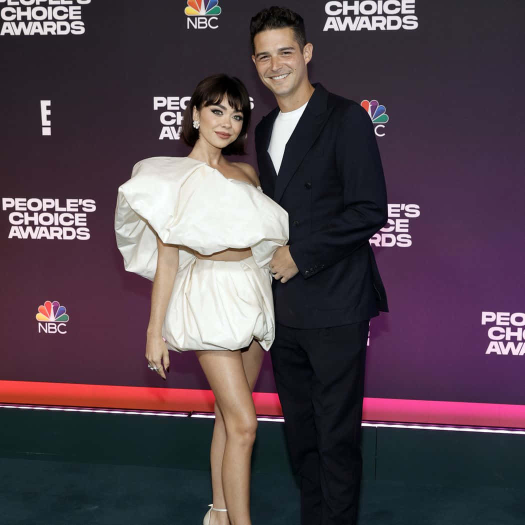 Sarah Hyland 桌布 壁紙 — 一對微笑的情侶在人民選擇獎的紅地毯上擺姿勢，背景為紫色和標誌。