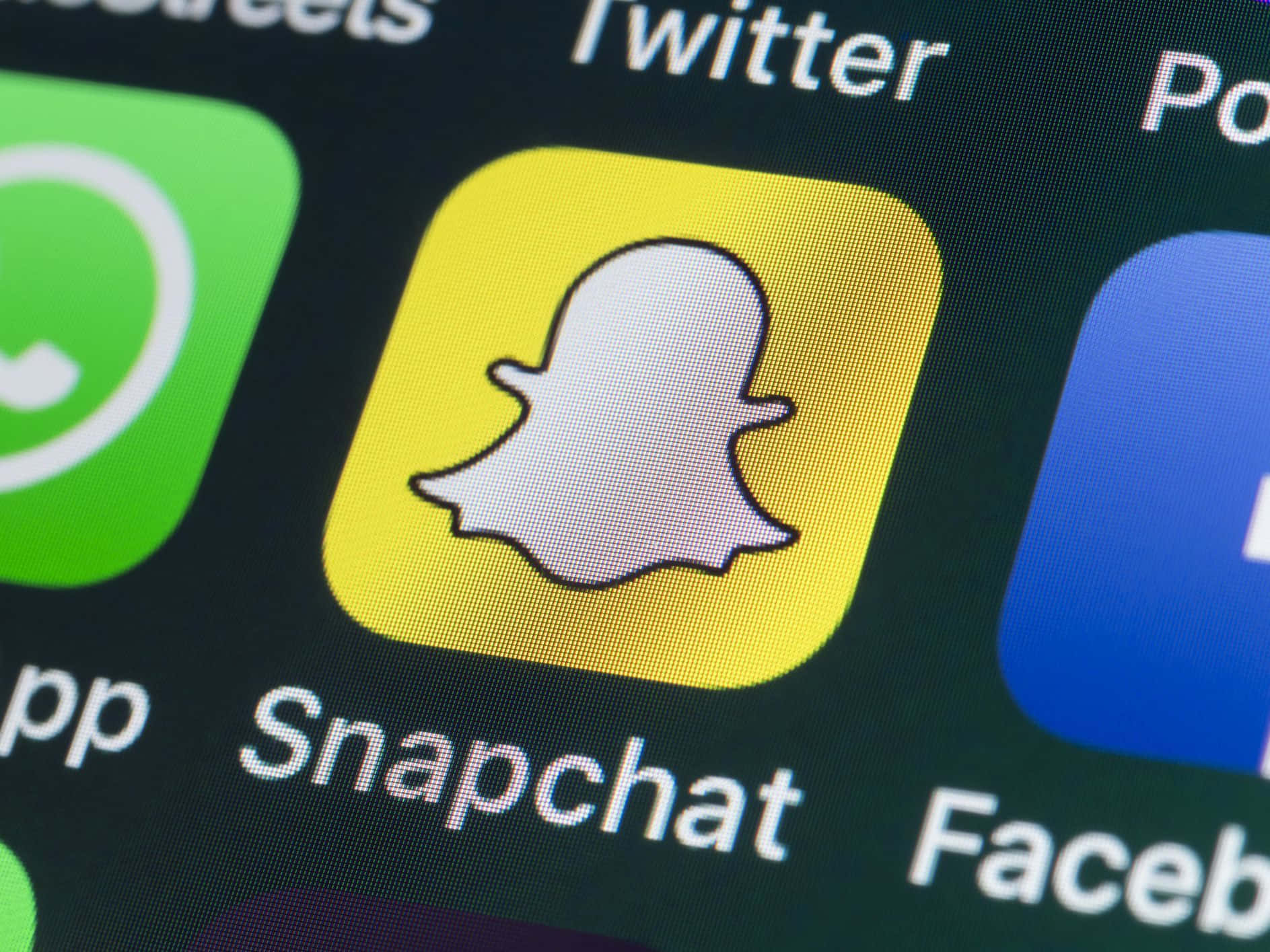 Snapchat 桌布 壁紙 — Snapchat應用程式圖標在智慧型手機螢幕上發出黃色光芒的特寫，周圍環繞著其他社交媒體應用程式。