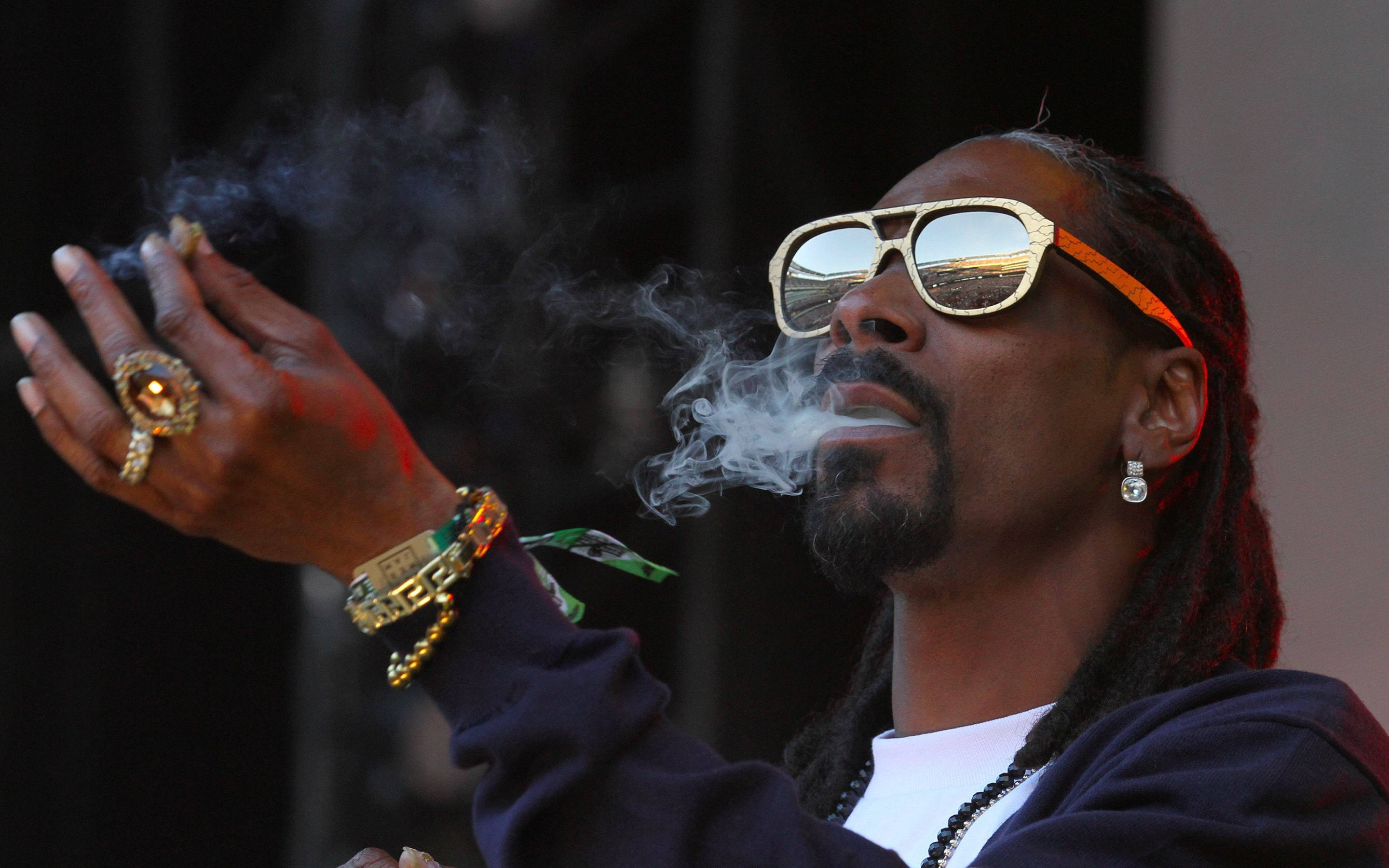 Snoop Dogg 桌布 壁紙 — Snoop Dogg 在深色背景下戴著金邊太陽眼鏡和閃亮珠寶呼出煙霧。