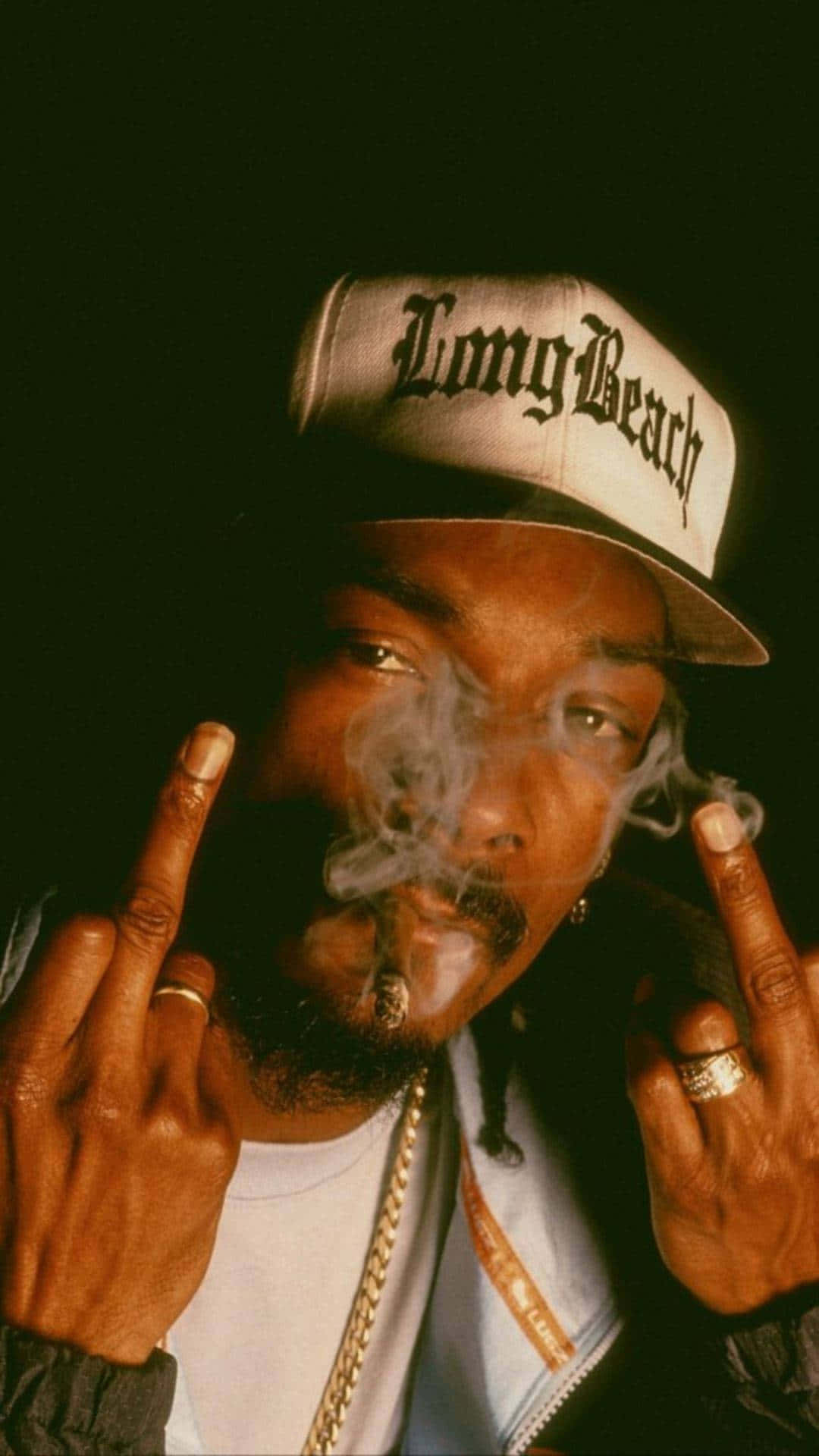 Young Snoop Dogg 桌布 壁紙 — Snoop Dogg 在深色背景前戴著 Long Beach 帽子，舉起雙手中指並呼出煙霧。