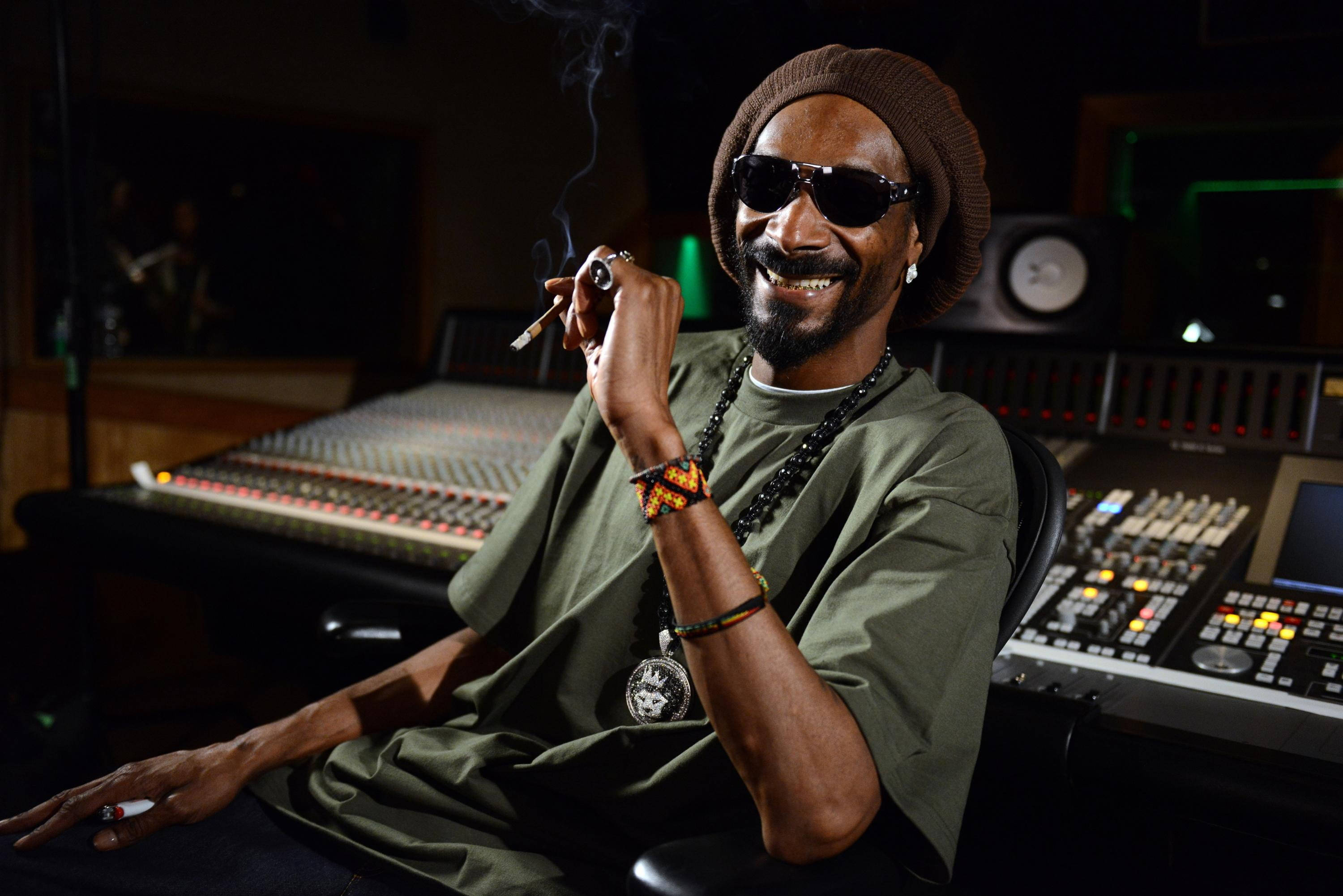 Snoop 桌布 壁紙 — Snoop Dogg 在燈光昏暗的錄音室中，被音響設備包圍，一邊吸煙一邊微笑。