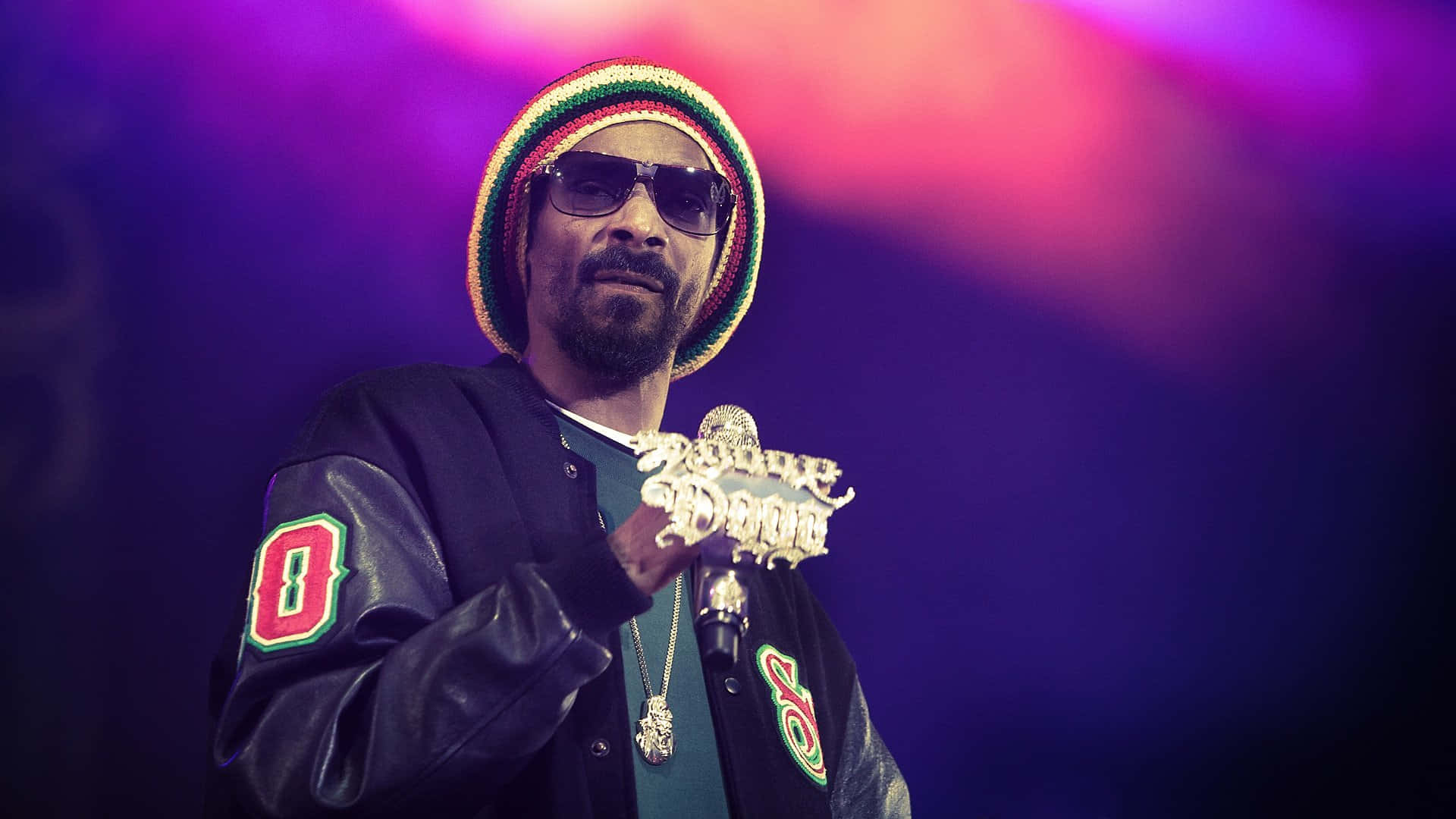 Young Snoop Dogg 桌布 壁紙 — Snoop Dogg 戴著色彩繽紛的毛帽和皮夾克，在充滿活力的舞台燈光下拿著麥克風。