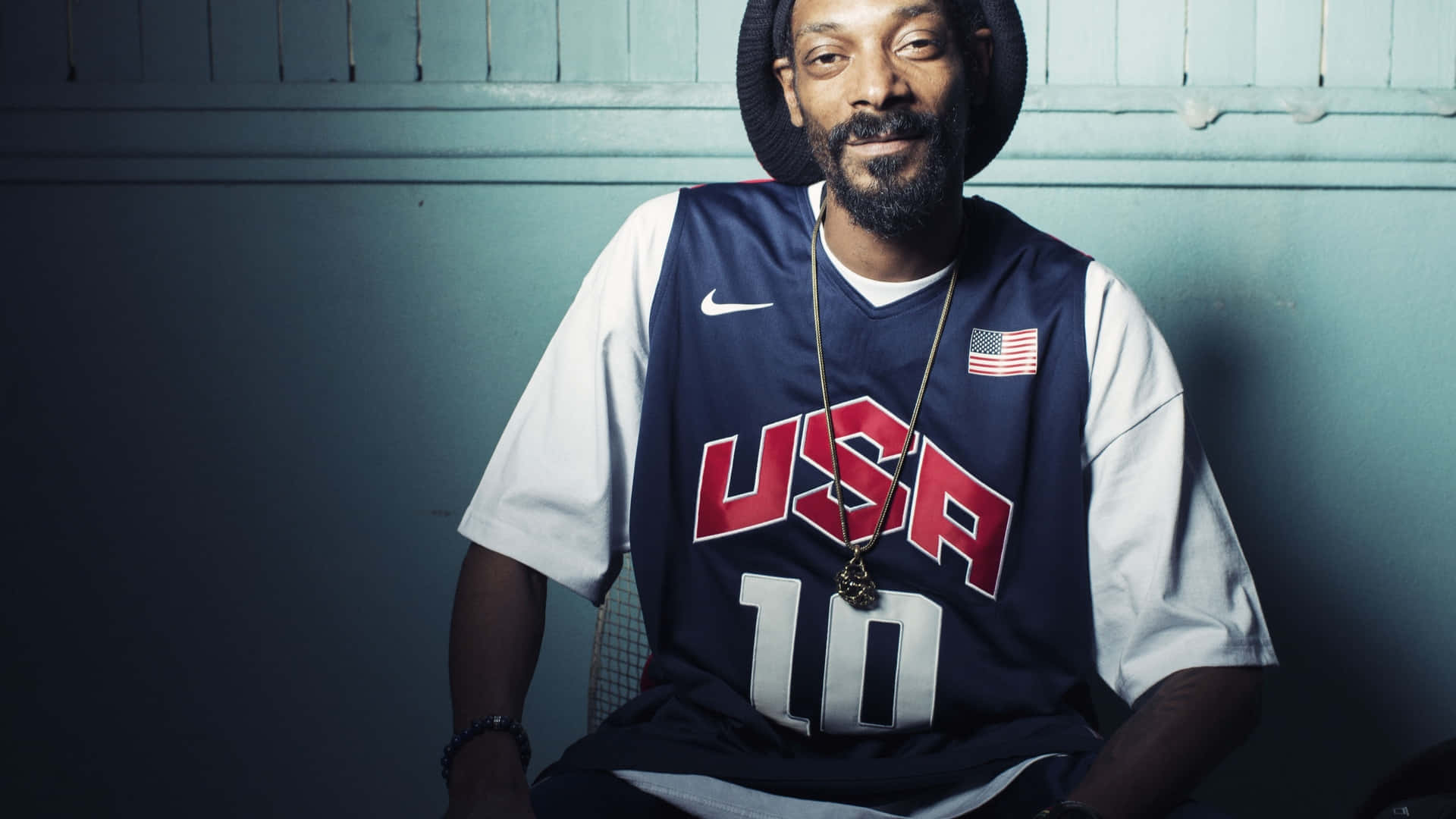 Young Snoop Dogg 桌布 壁紙 — Snoop Dogg 自信地坐在美國籃球球衣中，背景是青綠色鑲板牆，燈光效果戲劇化。