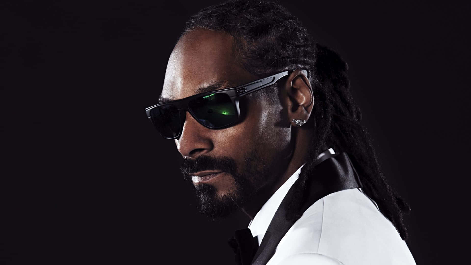 Rapper Pc 桌布 壁紙 — Snoop Dogg 身穿白色西裝和黑色太陽眼鏡，在深色背景前自信地微笑擺姿勢。