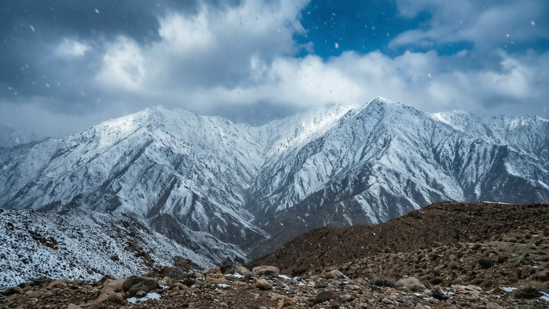 Tabuk Snowy Peaks 壁紙 — 白雪覆蓋著鋸齒狀的山峰，天空戲劇性，有旋轉的雲和飄落的雪花。