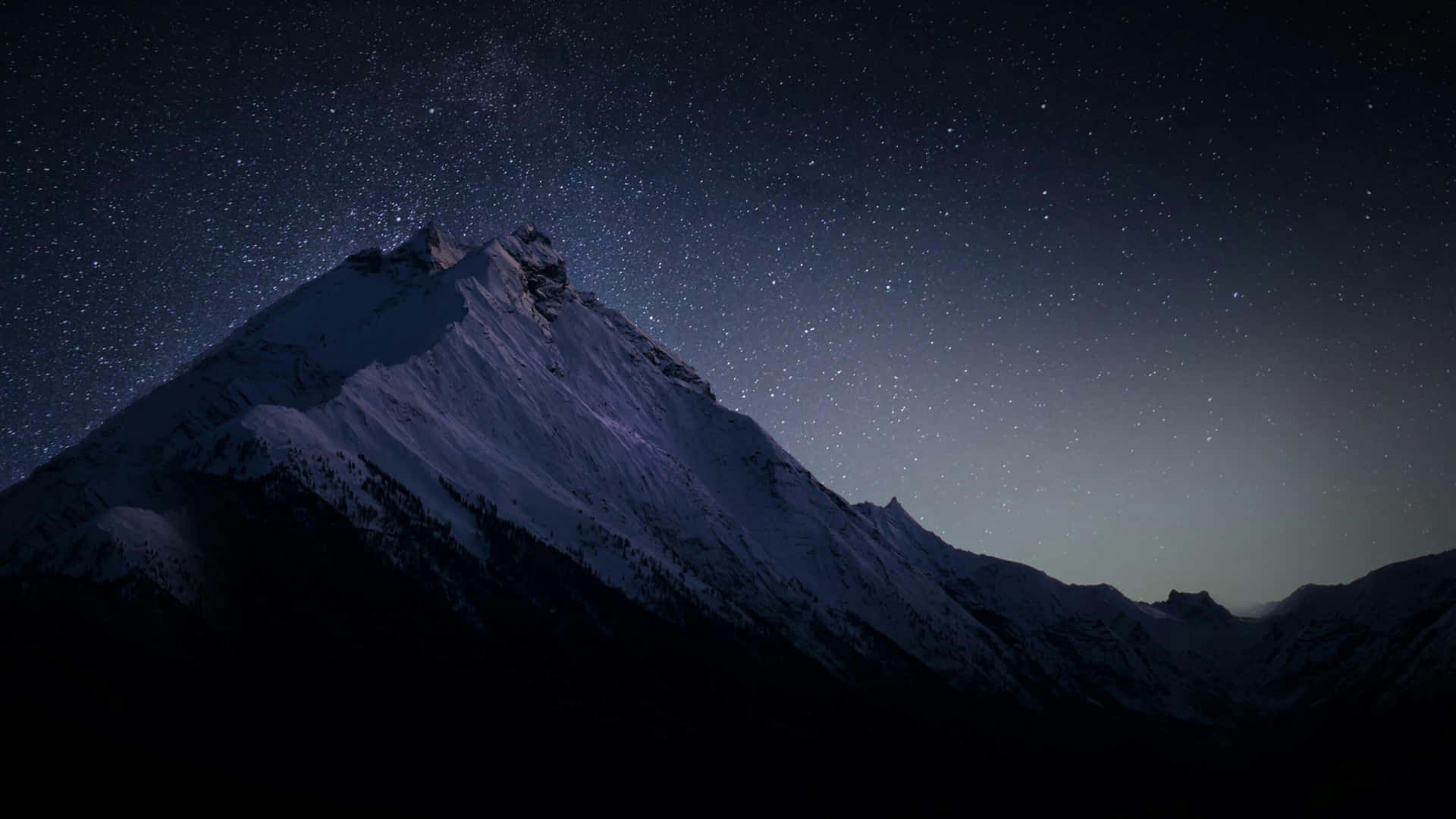  壁紙 — 白雪覆蓋的山峰在繁星點點的夜空下升起，地平線上有微弱的極光。