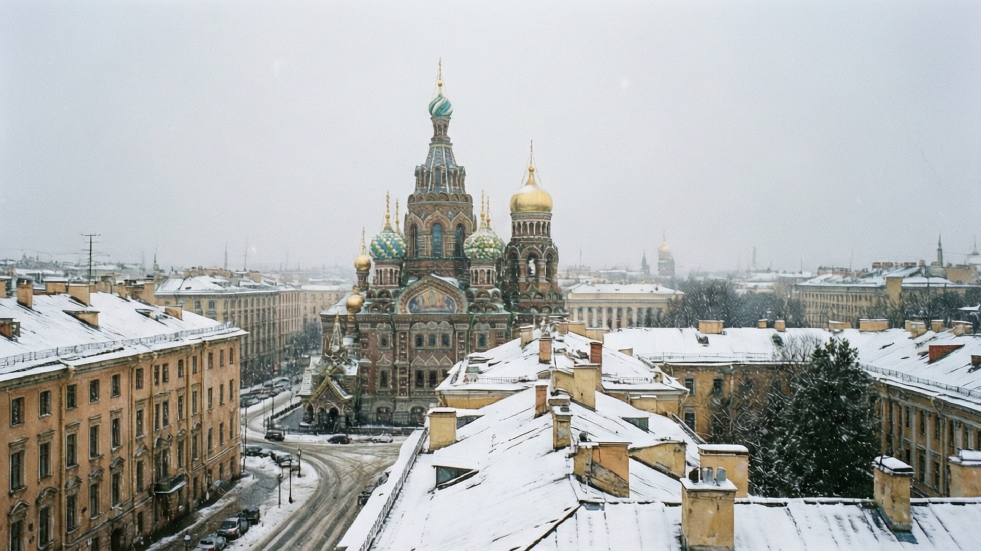 Snowy Cityscape 壁紙 — 白雪覆蓋屋頂和街道，滴血救世主教堂的金色圓頂聳立在聖彼得堡的歷史天際線上。