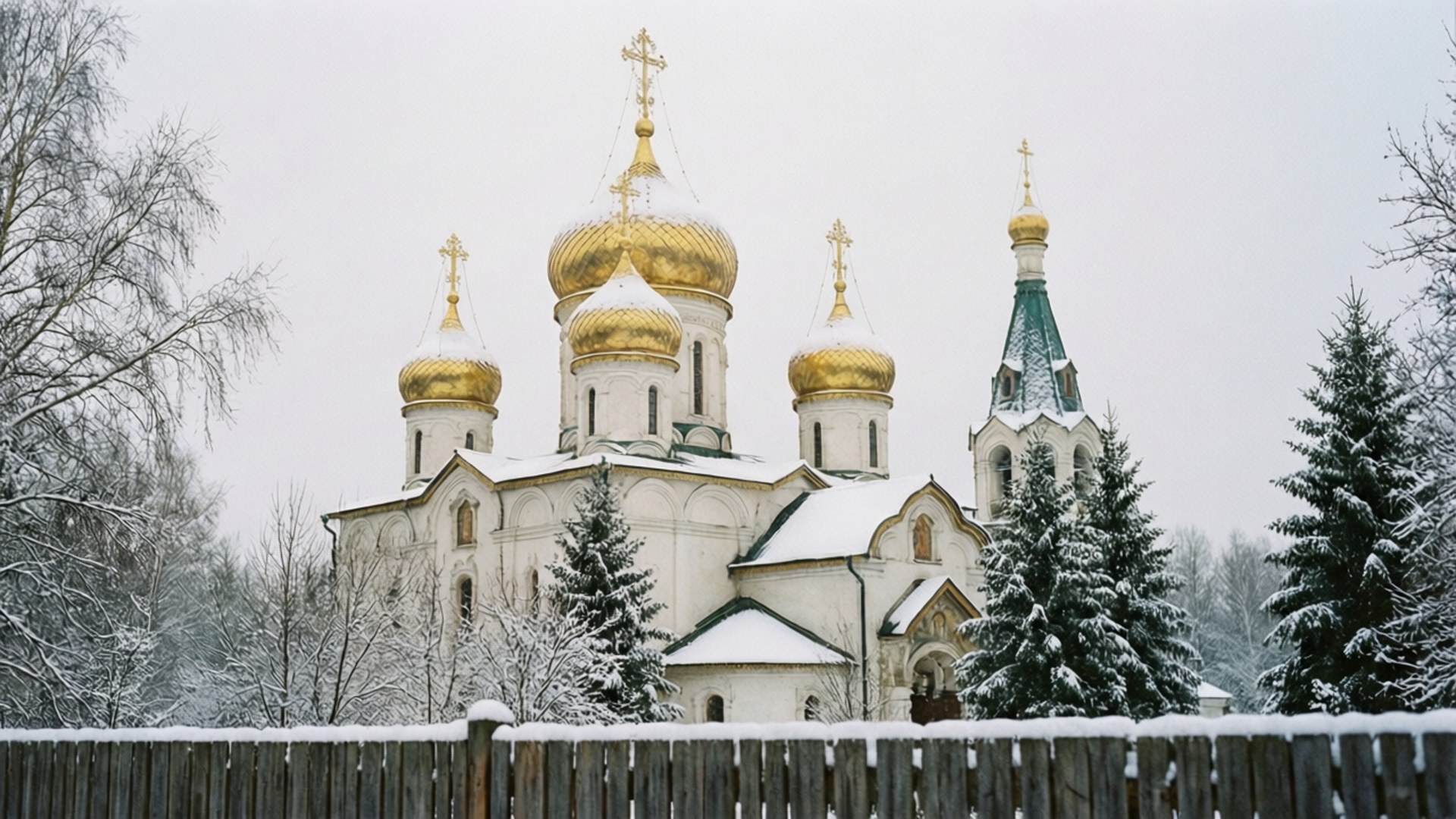 Snowy Onion Domes 壁紙 — 一座被雪覆蓋的俄羅斯東正教教堂，金色圓頂和十字架，在冬季樹木中寧靜地矗立在木柵欄後面。