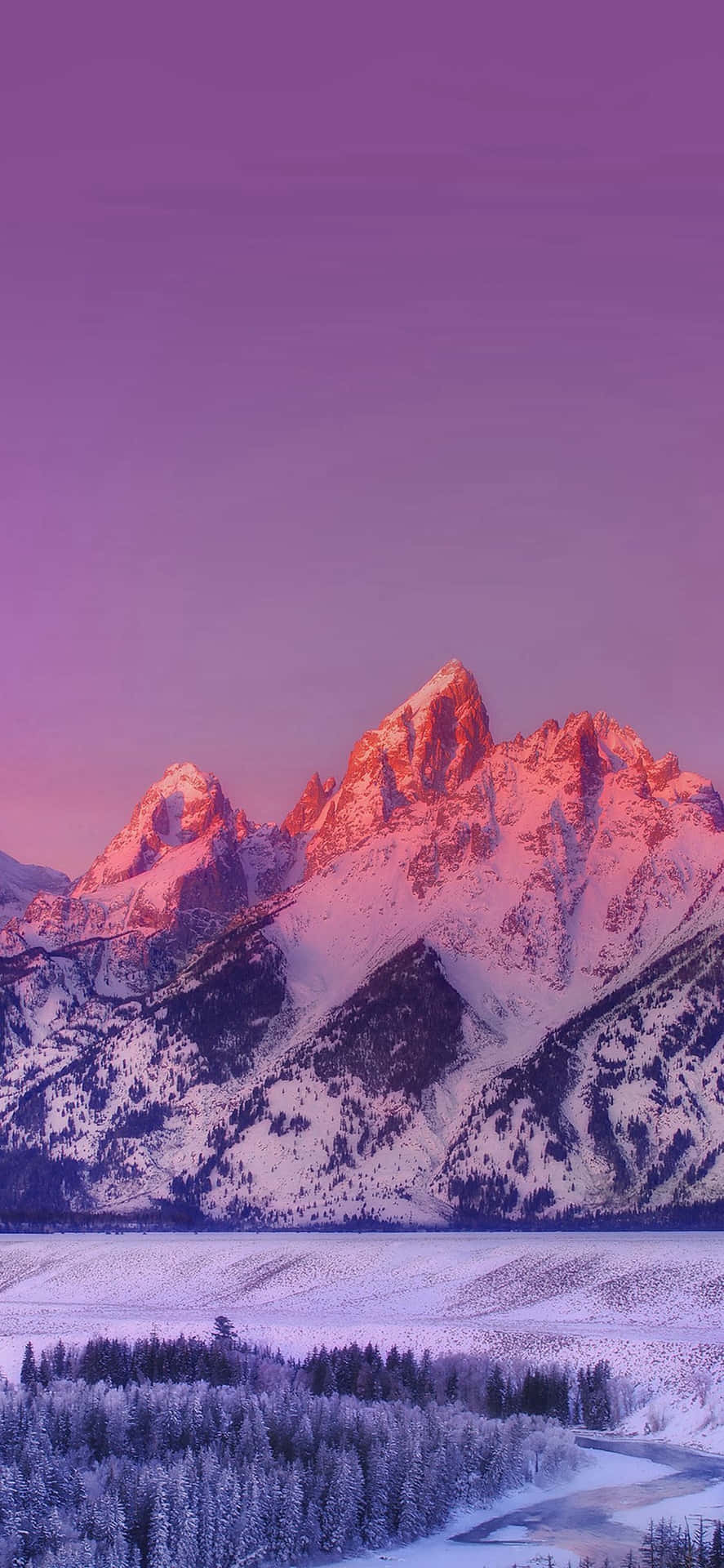 白雪覆蓋的山脈在日落時分呈現粉紅色和紫色，映照在冰凍的湖泊和森林之上。 — iPhone X 壁紙