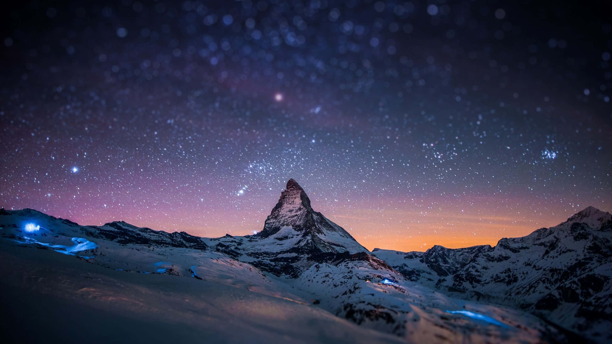 白雪覆蓋的山峰在紫色和橙色色調的星空暮色天空下。 — Macbook Pro 壁紙