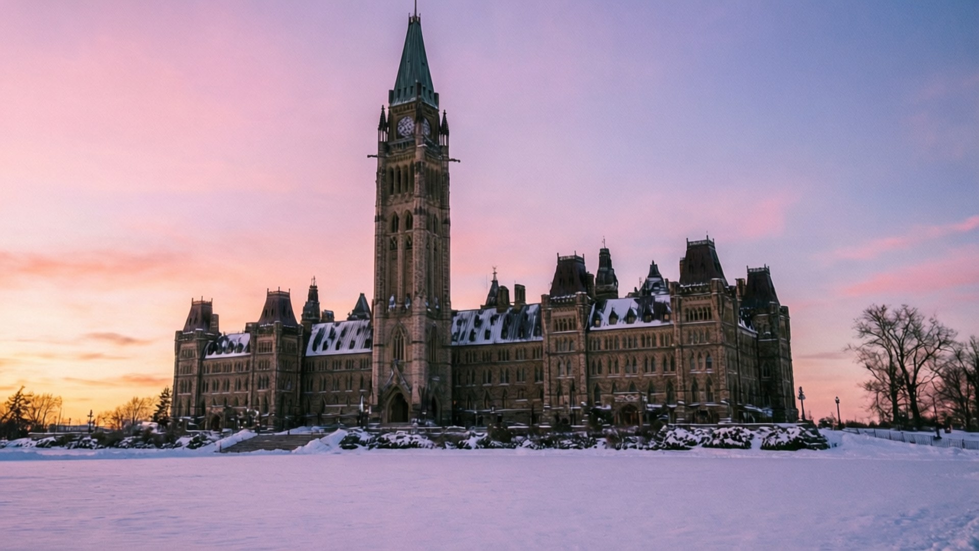 Snowy Parliament Hill 壁紙 — 一座宏偉的石造議會大樓，高聳的鐘樓在粉紅和紫色的日落天空下顯得莊嚴，周圍是白雪覆蓋的場地。