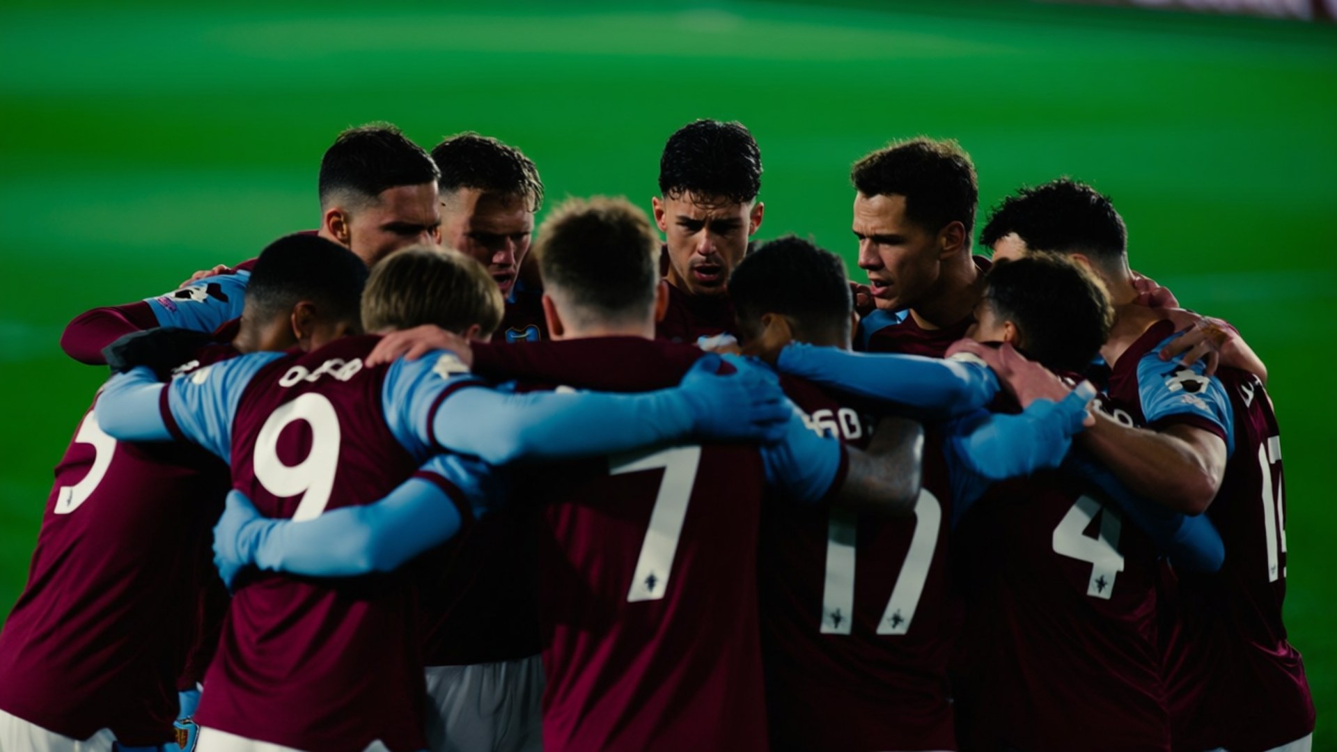 Team Huddle Before Match 壁紙 — 身穿栗色球衣的足球運動員在體育場燈光下緊密地聚集在充滿活力的綠色球場上。