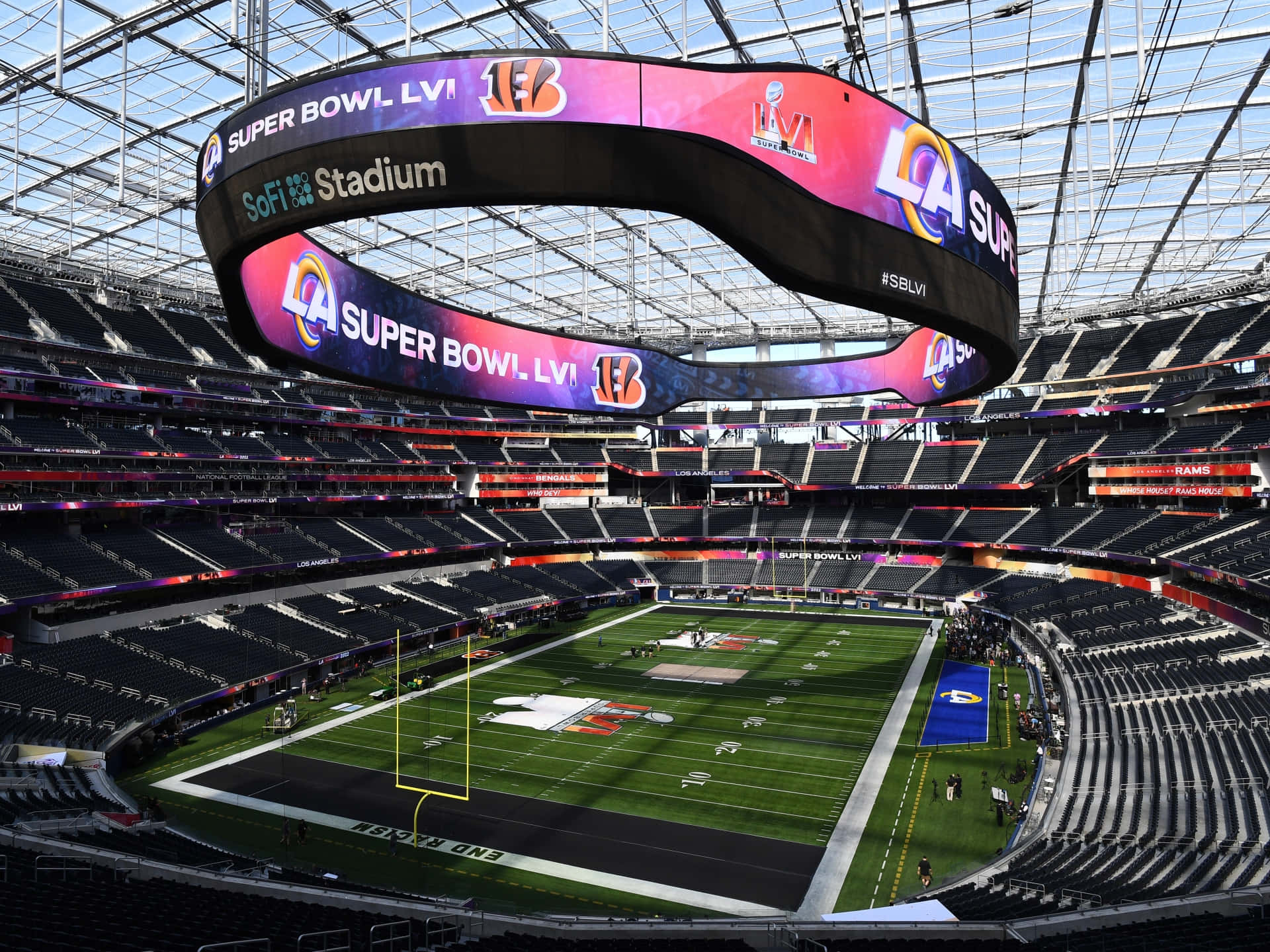 Sofi Stadium 桌布 壁紙 — SoFi 體育場在超級碗LVI期間的鳥瞰圖，鮮豔的紫色、粉紅色和藍色LED標牌懸掛在空蕩蕩的綠色足球場上方。