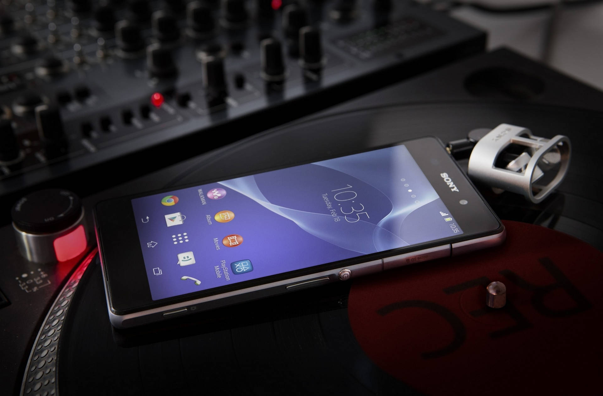 Sony手機放在黑膠唱片上，旁邊是帶紅燈的DJ混音器。 — iPhone 11 壁紙