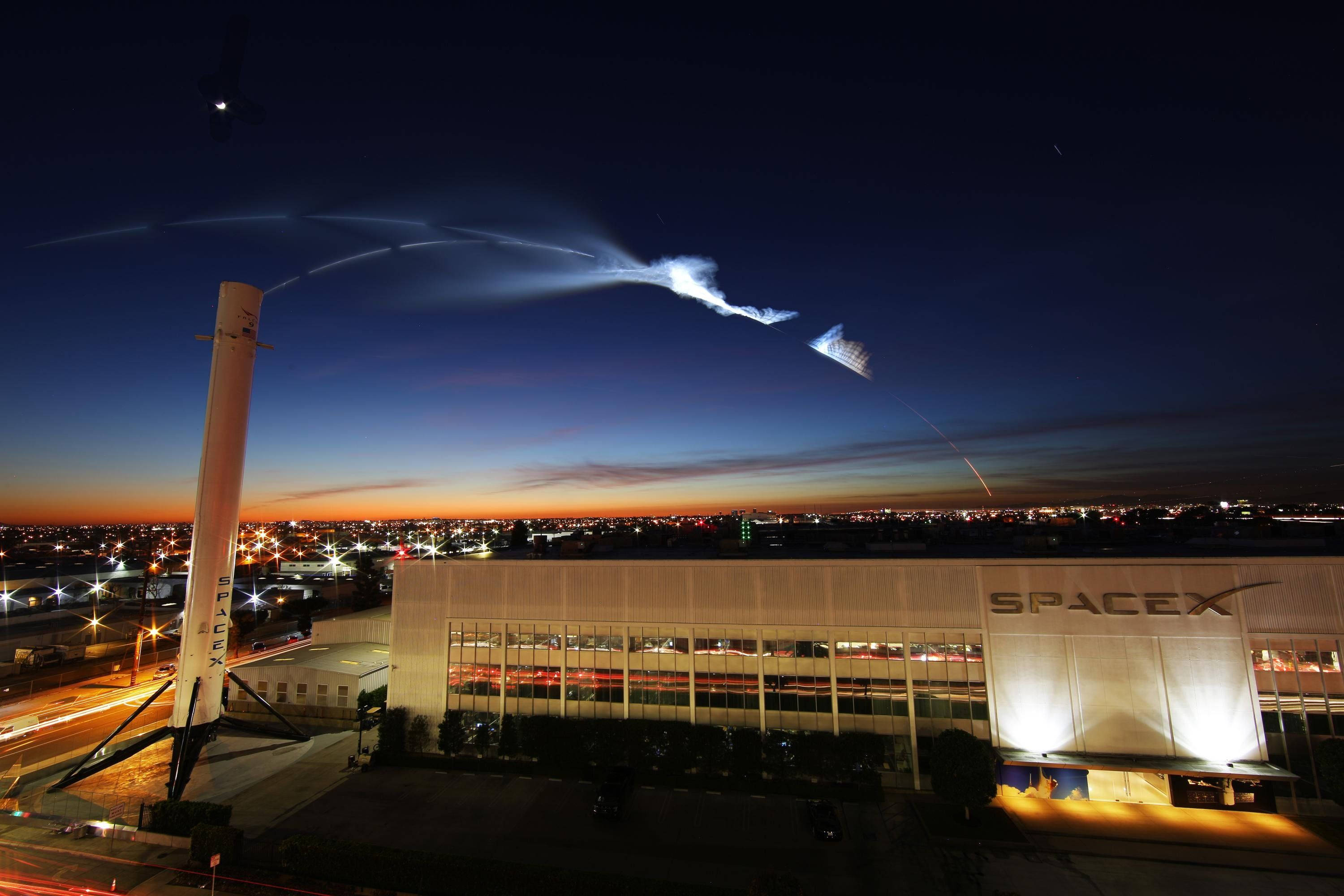 SpaceX 桌布 壁紙 — SpaceX 火箭在黃昏時升空，留下一道明亮的軌跡，下方是燈火通明的設施和城市燈光。