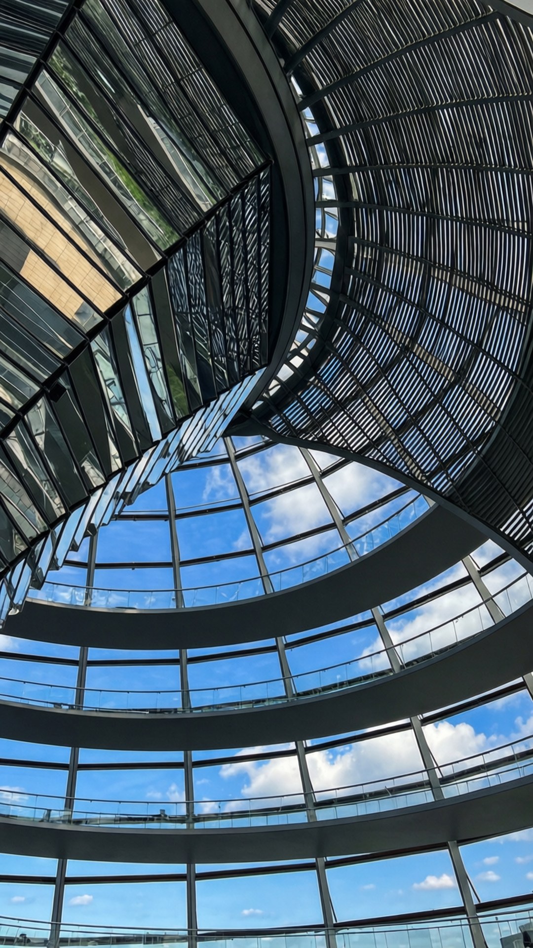 Reichstag Dome View 壁紙 — 螺旋形玻璃和鋼製圓頂通過其彎曲的透明面板顯露出明亮的藍天和蓬鬆的白雲。