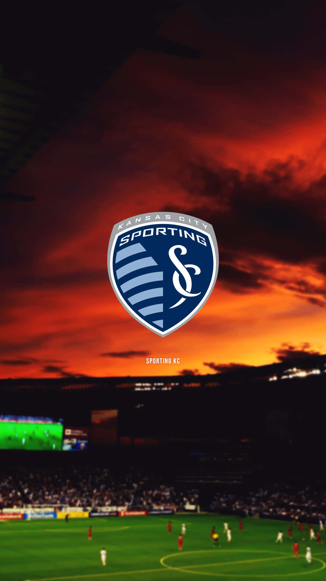足球 桌布 壁紙 — Sporting KC 標誌居中，背景是黃昏時分擠滿人的足球場上空熾熱的日落天空。