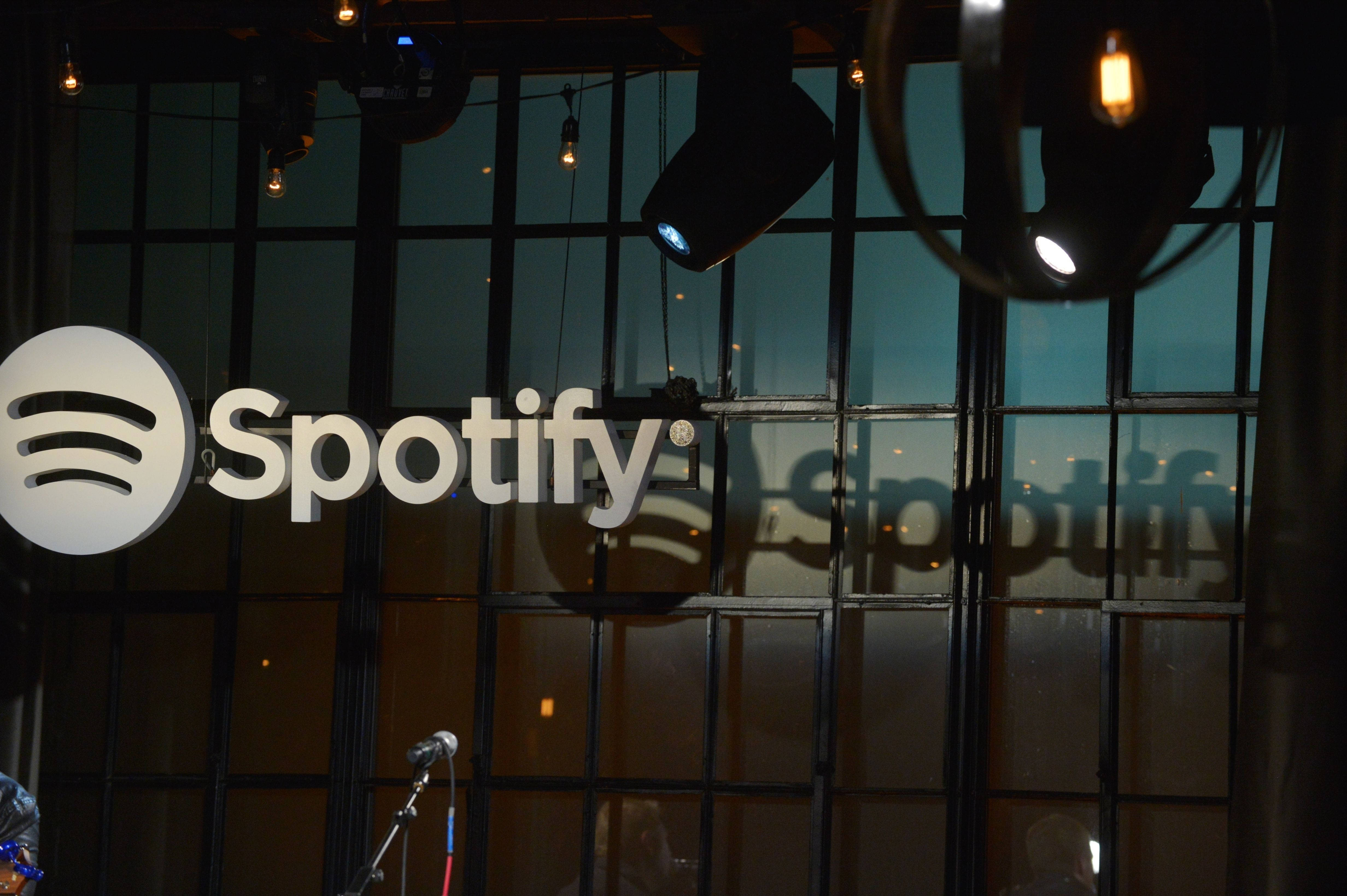 Spotify 桌布 壁紙 — Spotify 標誌在深色玻璃牆上以白色亮起，配有懸掛舞台燈和麥克風支架。