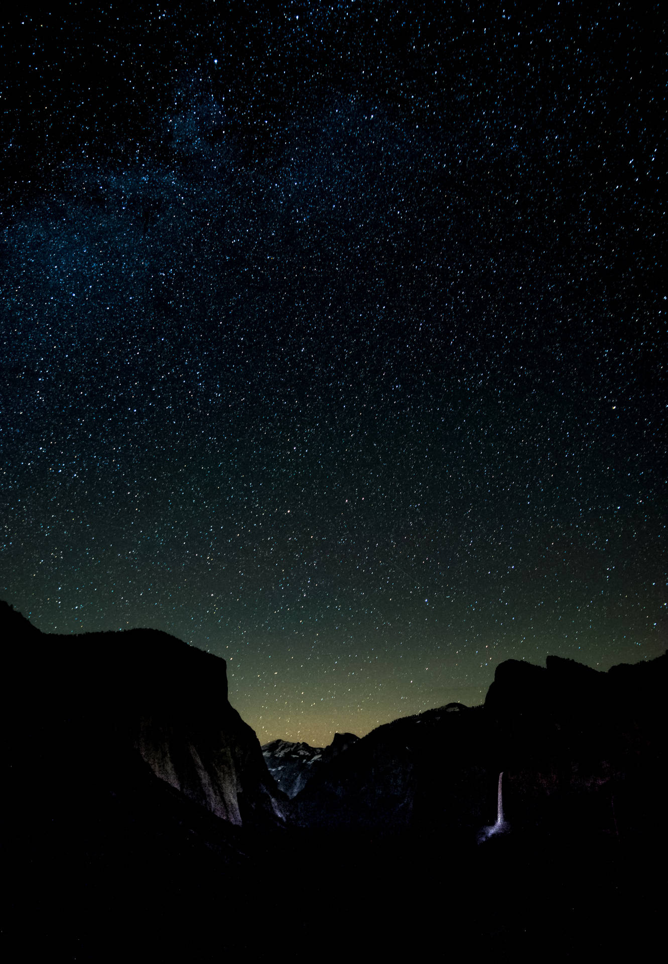 黑暗山脈在星空夜空和銀河下框住發光瀑布。 — iPhone 11 壁紙