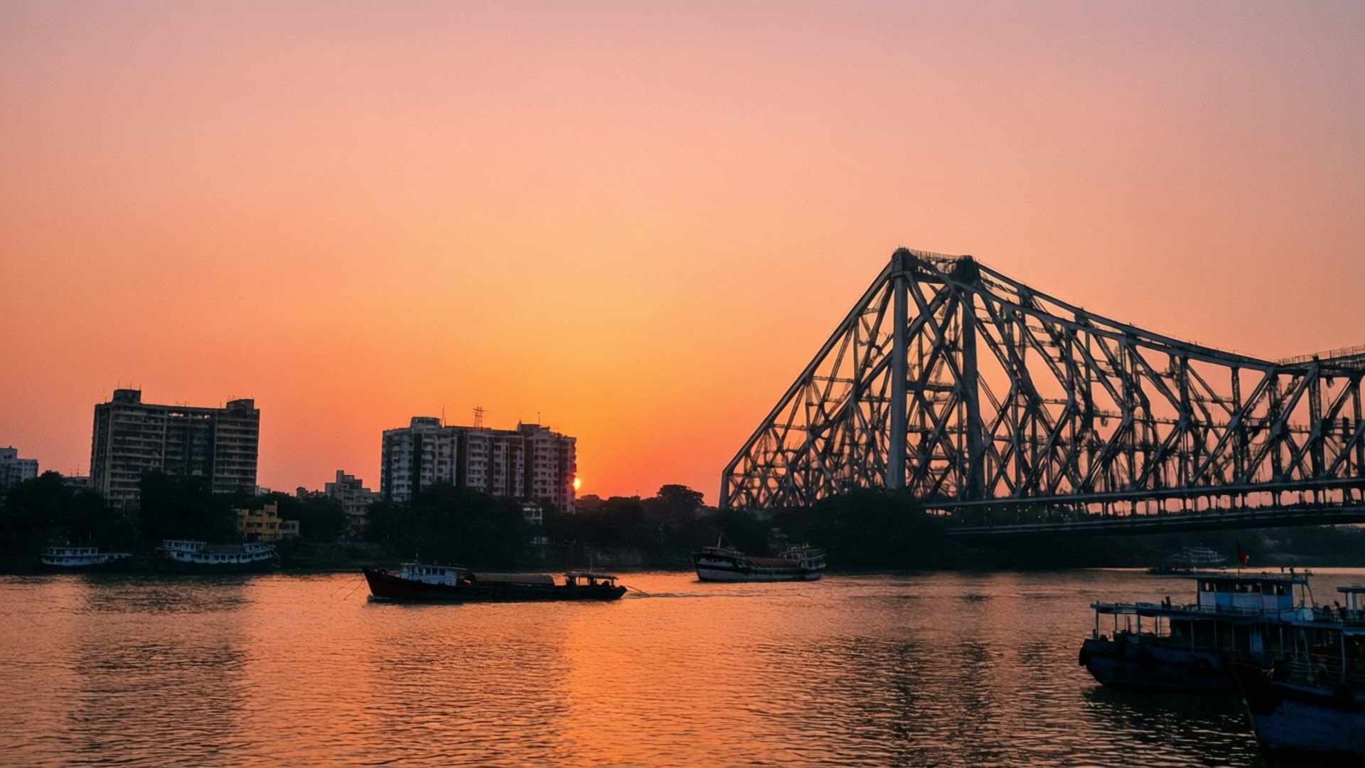 River Sunset Skyline 壁紙 — 一座鋼鐵桁架橋在河上以火熱橙色日落為背景形成剪影，遠處有船隻和城市建築。