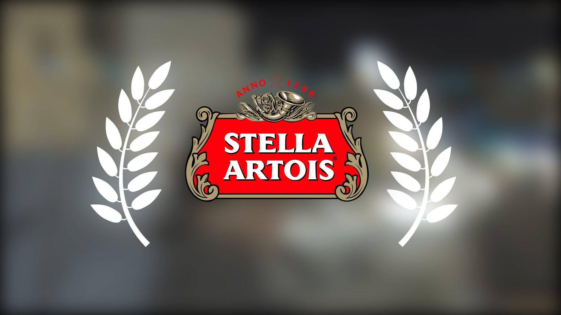 飲料 桌布 壁紙 — Stella Artois 標誌，帶有華麗的金色邊框和白色月桂花環，背景模糊。