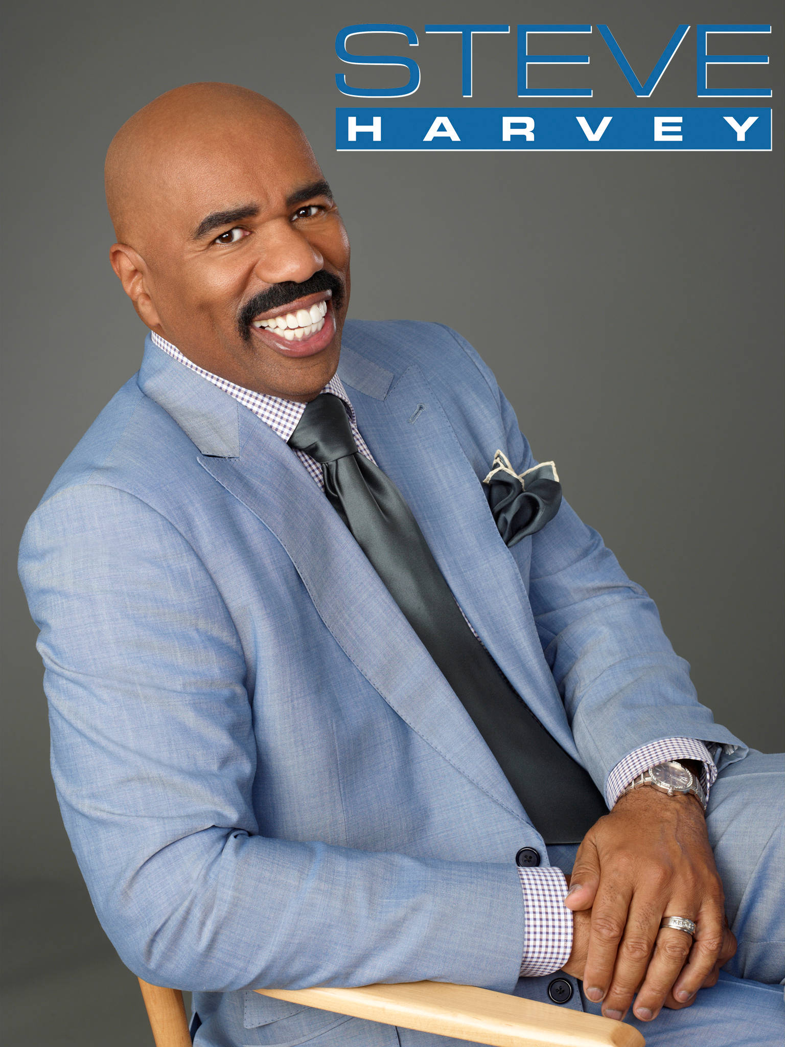 steve harvey 桌布 壁紙 — Steve Harvey 身穿亮麗淺藍色西裝，在灰色中性攝影棚背景下展露燦爛笑容。