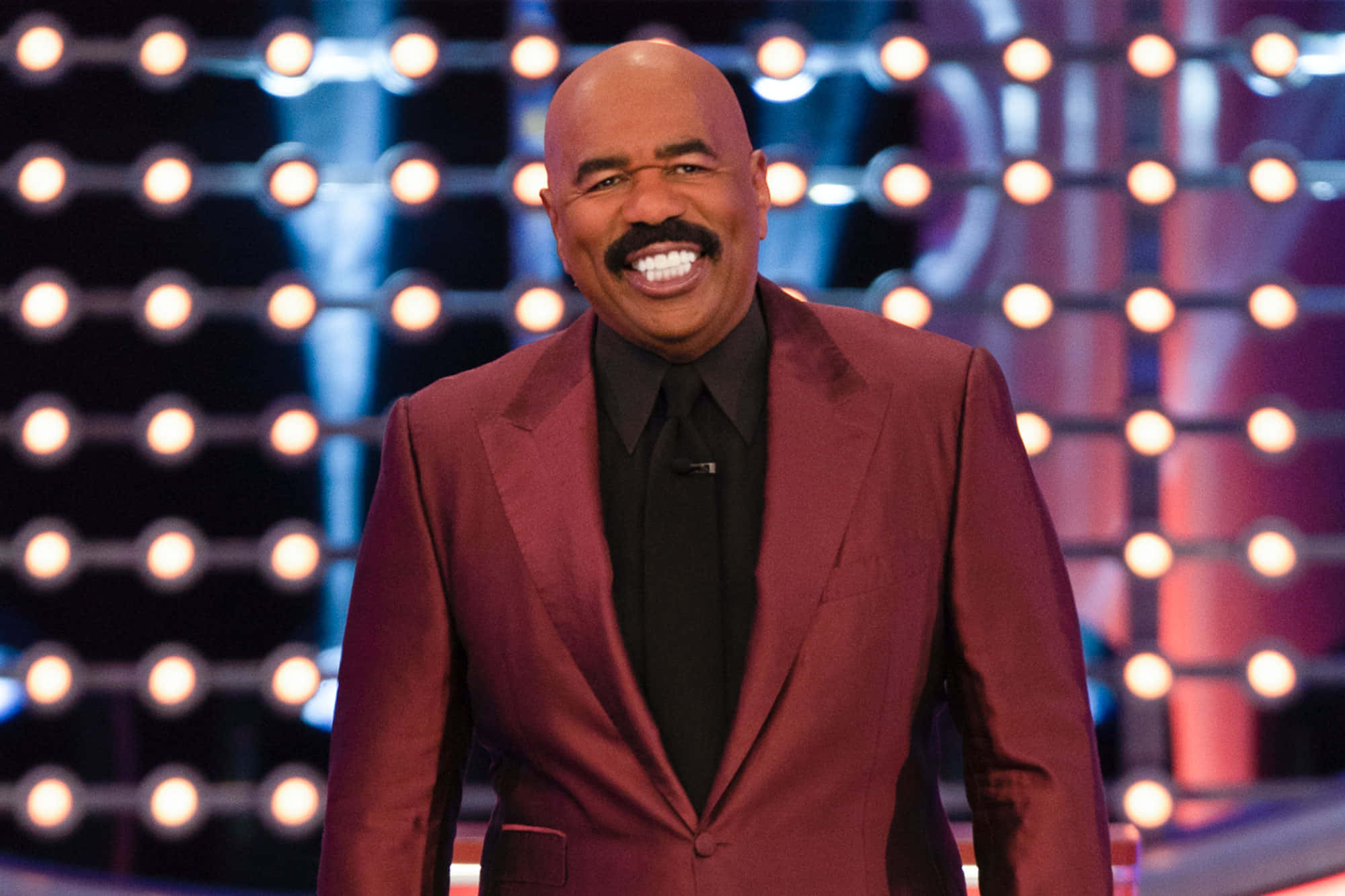 steve harvey 桌布 壁紙 — Steve Harvey 身穿栗色西裝，在閃爍的舞台燈光背景下綻放光芒。