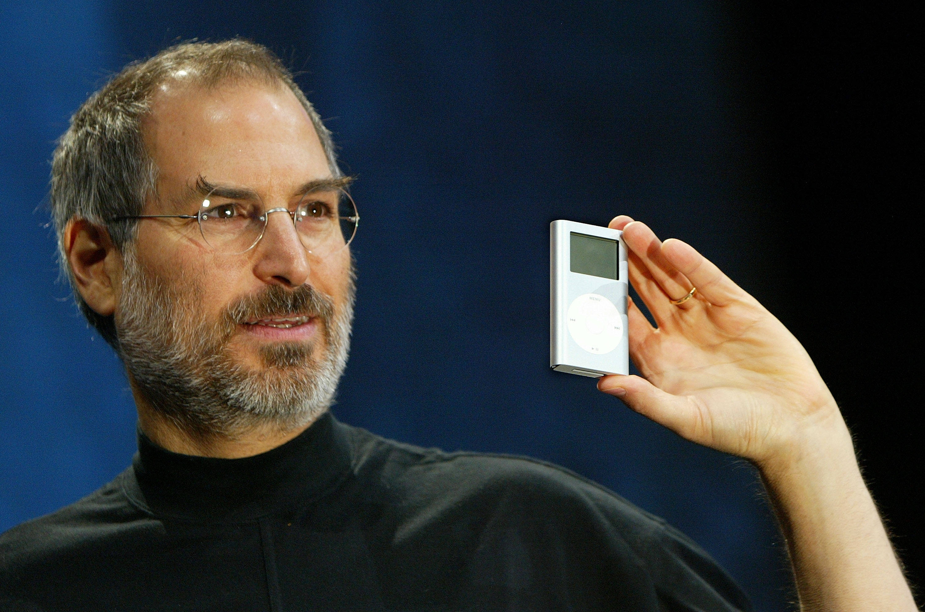Rich 桌布 壁紙 — Steve Jobs 在產品發表會上，手持白色 iPod，背景為深藍色。