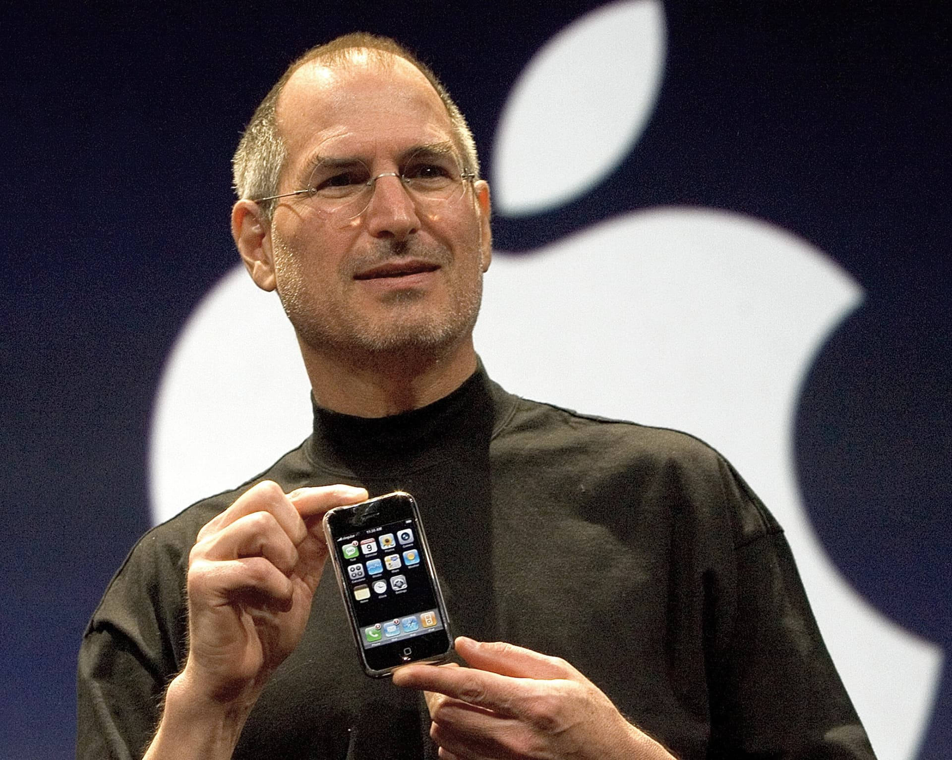 Rich 桌布 壁紙 — Steve Jobs 在舞台上舉起第一代 iPhone，背後是巨大的 Apple 標誌。
