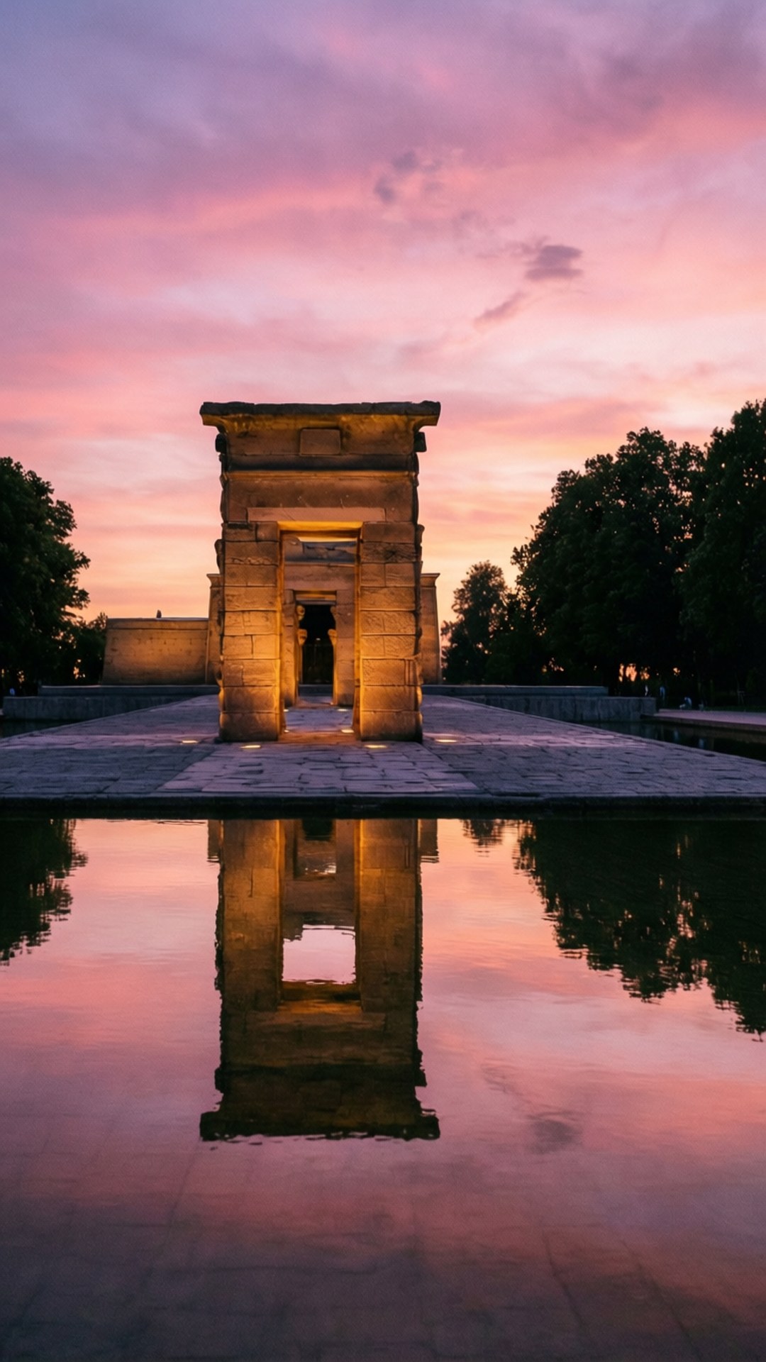 Debod Temple Sunset 壁紙 — 一座石廟大門在日落時被照亮，其倒影完美地映照在平靜的水面上，天空呈現粉紅色和紫色。