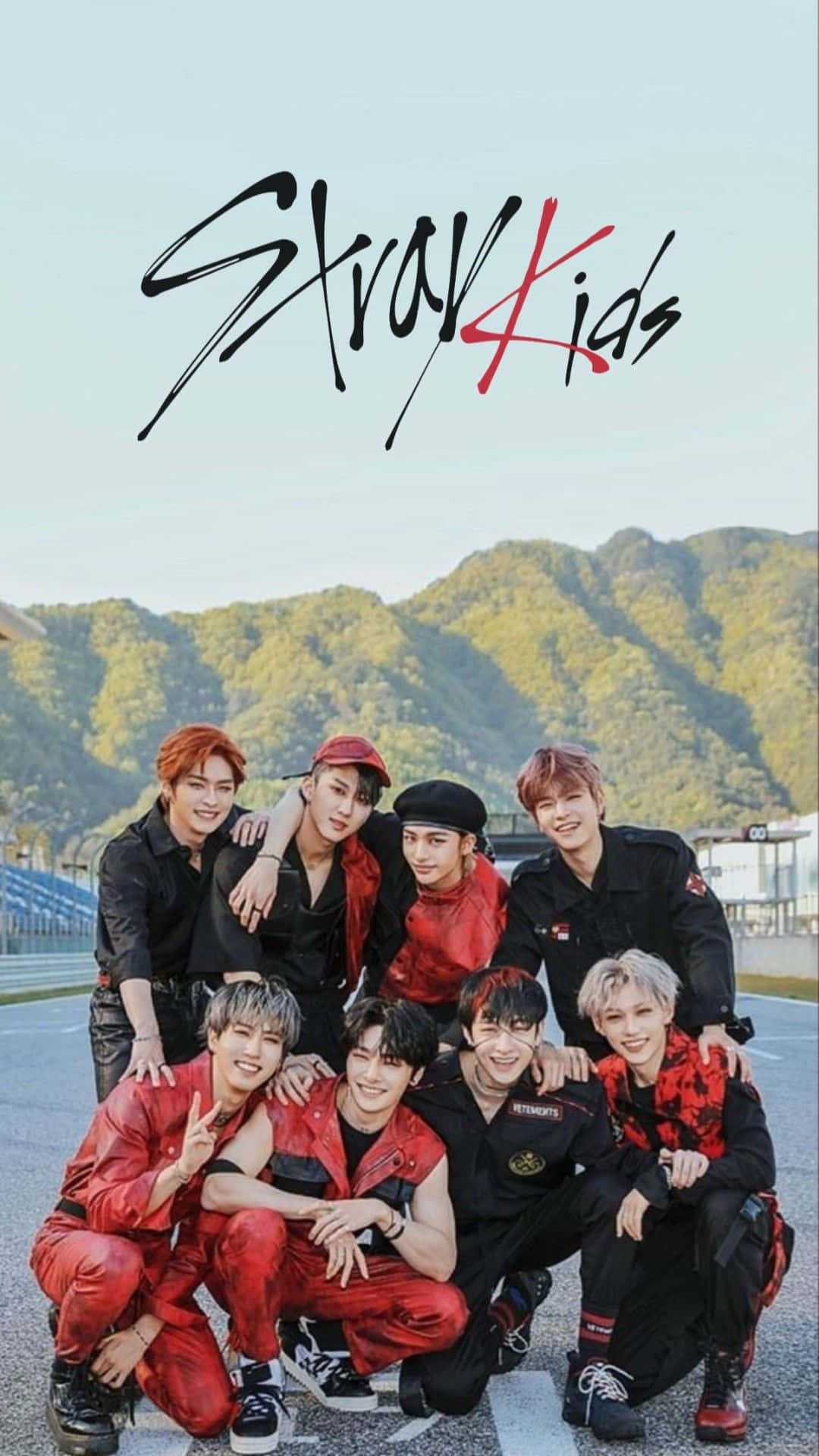桌布 壁紙 — Stray Kids 七位成員自信地穿著紅黑服裝，在賽車道上擺姿勢，背景是綠色的山脈。