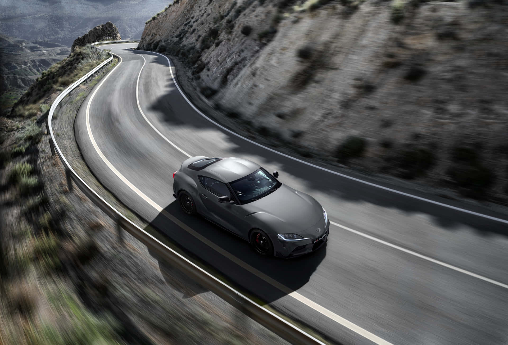 灰色跑車在蜿蜒的山路上疾馳（日落時分）。 — Toyota Supra 壁紙