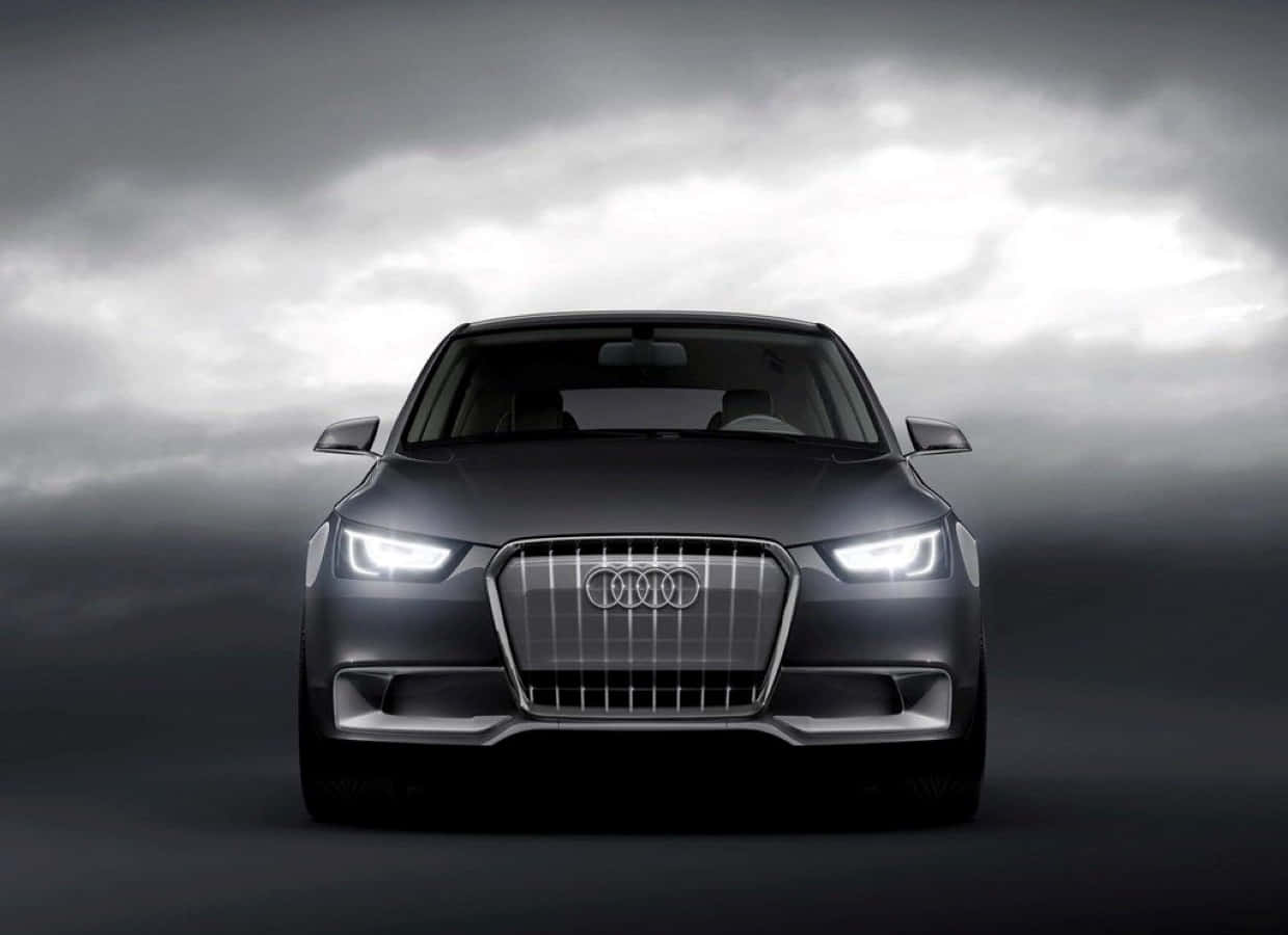 Audi A3 桌布 壁紙 — 一輛時尚的黑色奧迪汽車，帶有發光的車頭燈，在戲劇性的多雲天空下正面朝前。