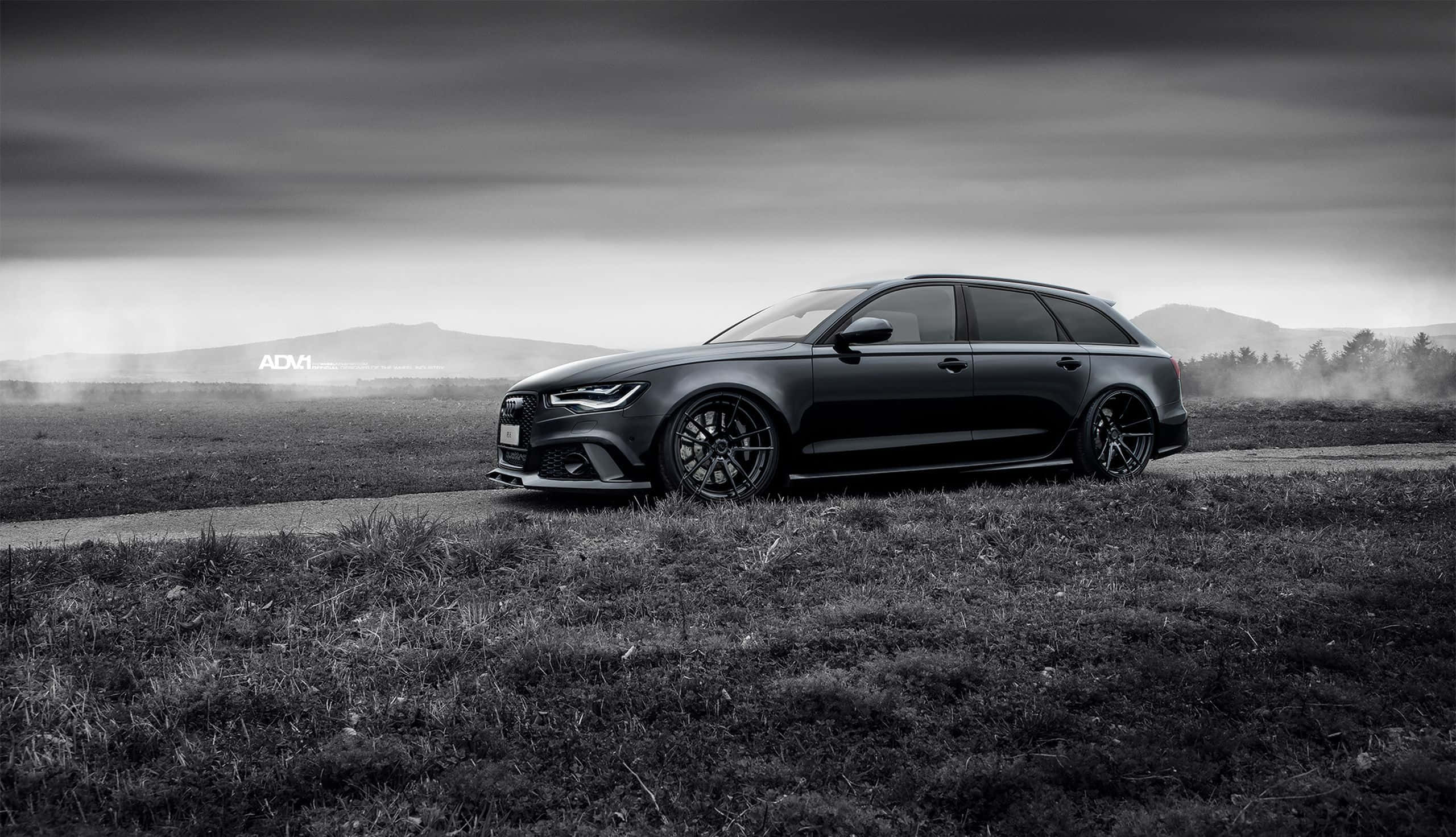 Audi Rs6 桌布 壁紙 — 一輛時尚的黑色奧迪RS6 Avant旅行車停在鄉間小路上，背景是霧氣繚繞的山丘，天空陰沉而富有戲劇性。