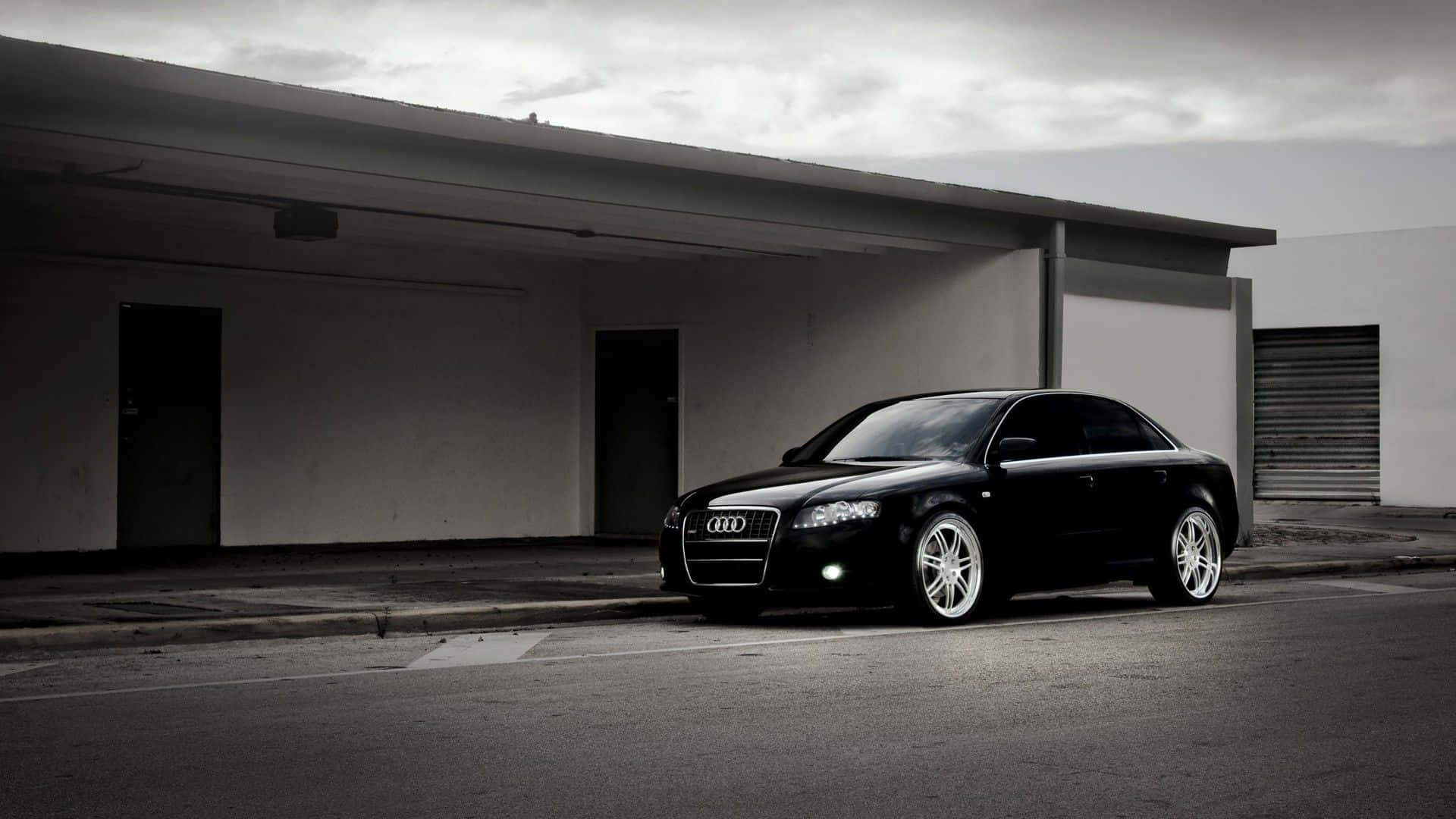 Audi A4 桌布 壁紙 — 一輛時尚的黑色奧迪轎車配備定制輪圈，在陰天停放在現代混凝土簷篷下。