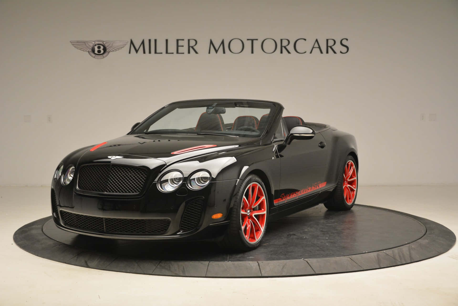 Bentley Continental Supersports 桌布 壁紙 — 一輛時尚的黑色賓利敞篷車，配以鮮豔的橙色車輪和裝飾，展示在極簡主義展廳的圓形平台上。