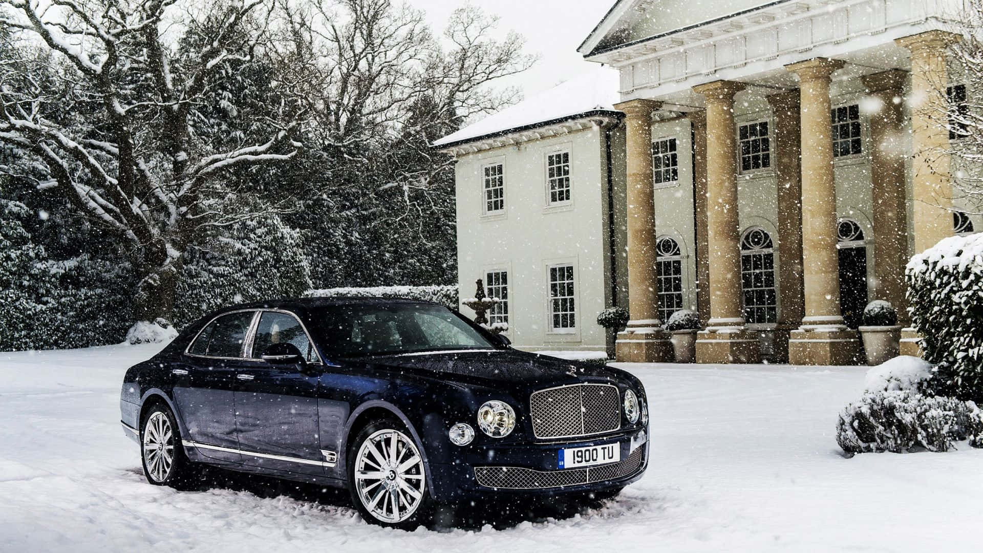 Bentley Mulsanne 桌布 壁紙 — 一輛時尚的黑色賓利轎車停在剛下的雪地上，前方是宏偉的柱式豪宅，雪花飄落。