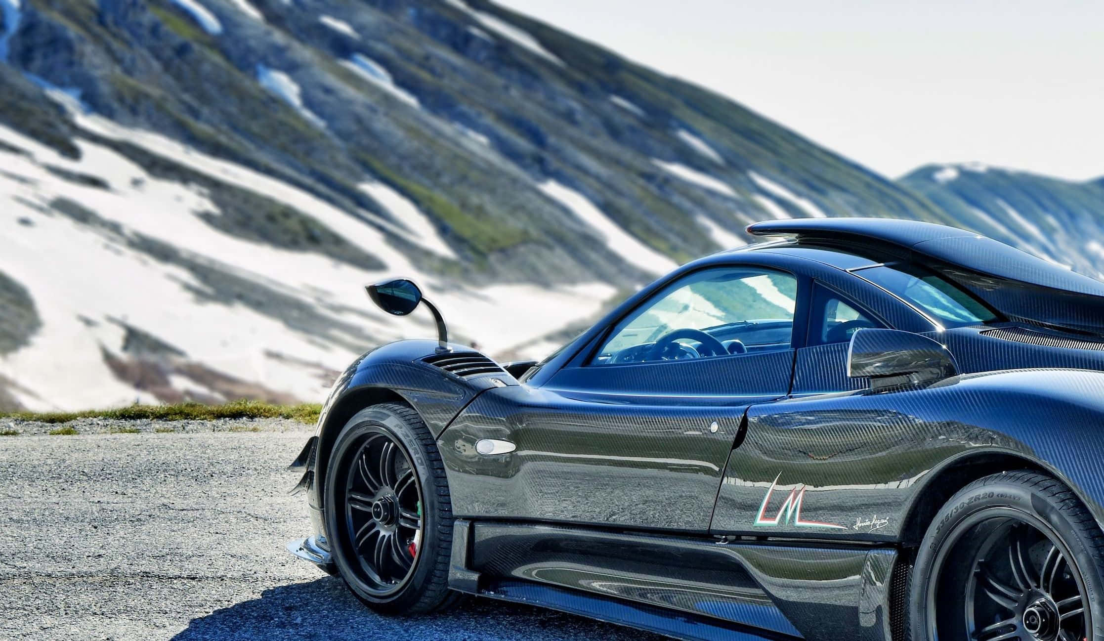 Pagani Zonda Hp Barchetta 桌布 壁紙 — 一輛時尚的黑色碳纖維跑車停泊在碎石路上，背景是白雪覆蓋的山脈。