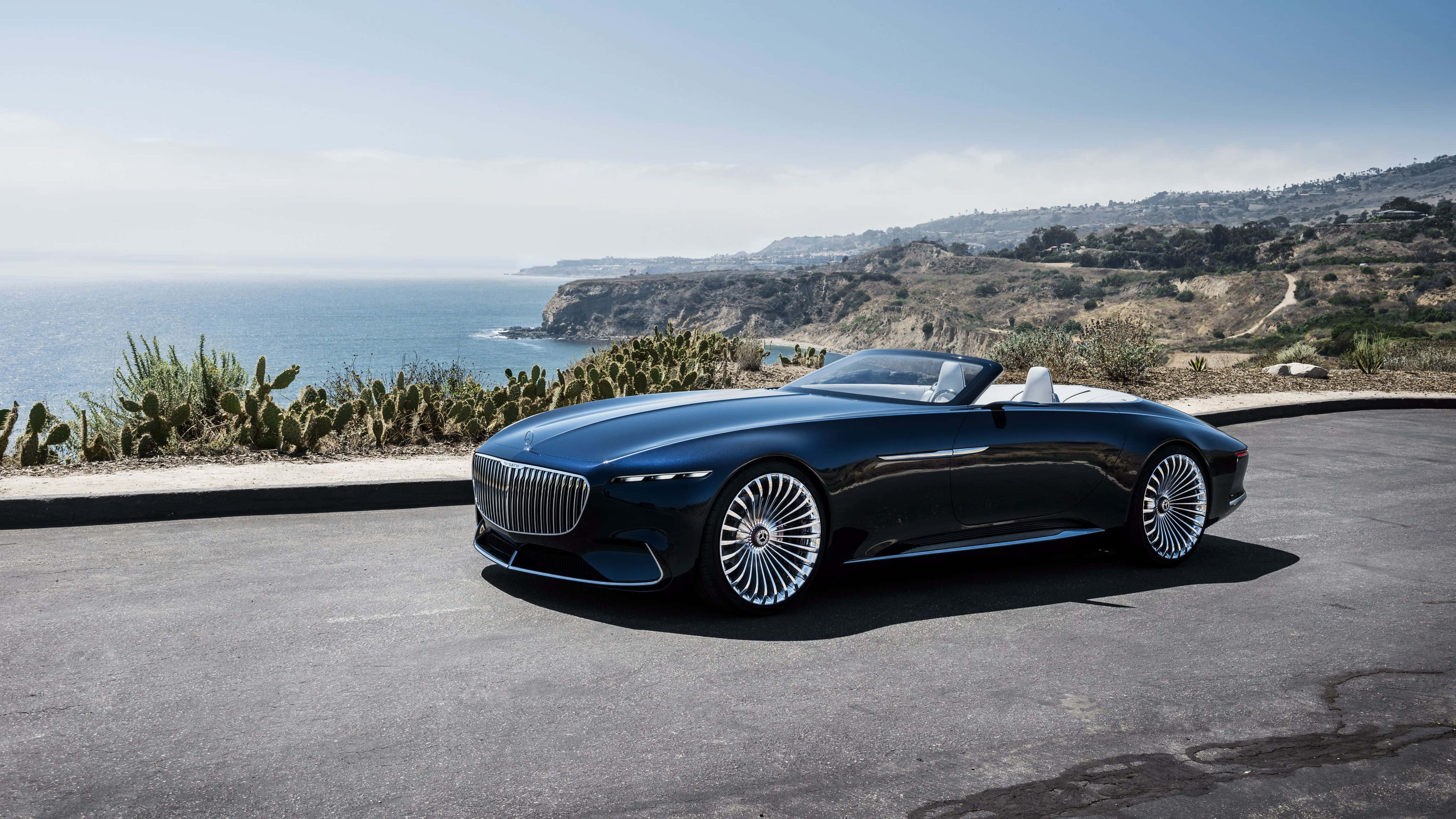Maybach 桌布 壁紙 — 一輛時尚黑色敞篷跑車停泊在沿海公路上，俯瞰海洋，背景有仙人掌和懸崖。