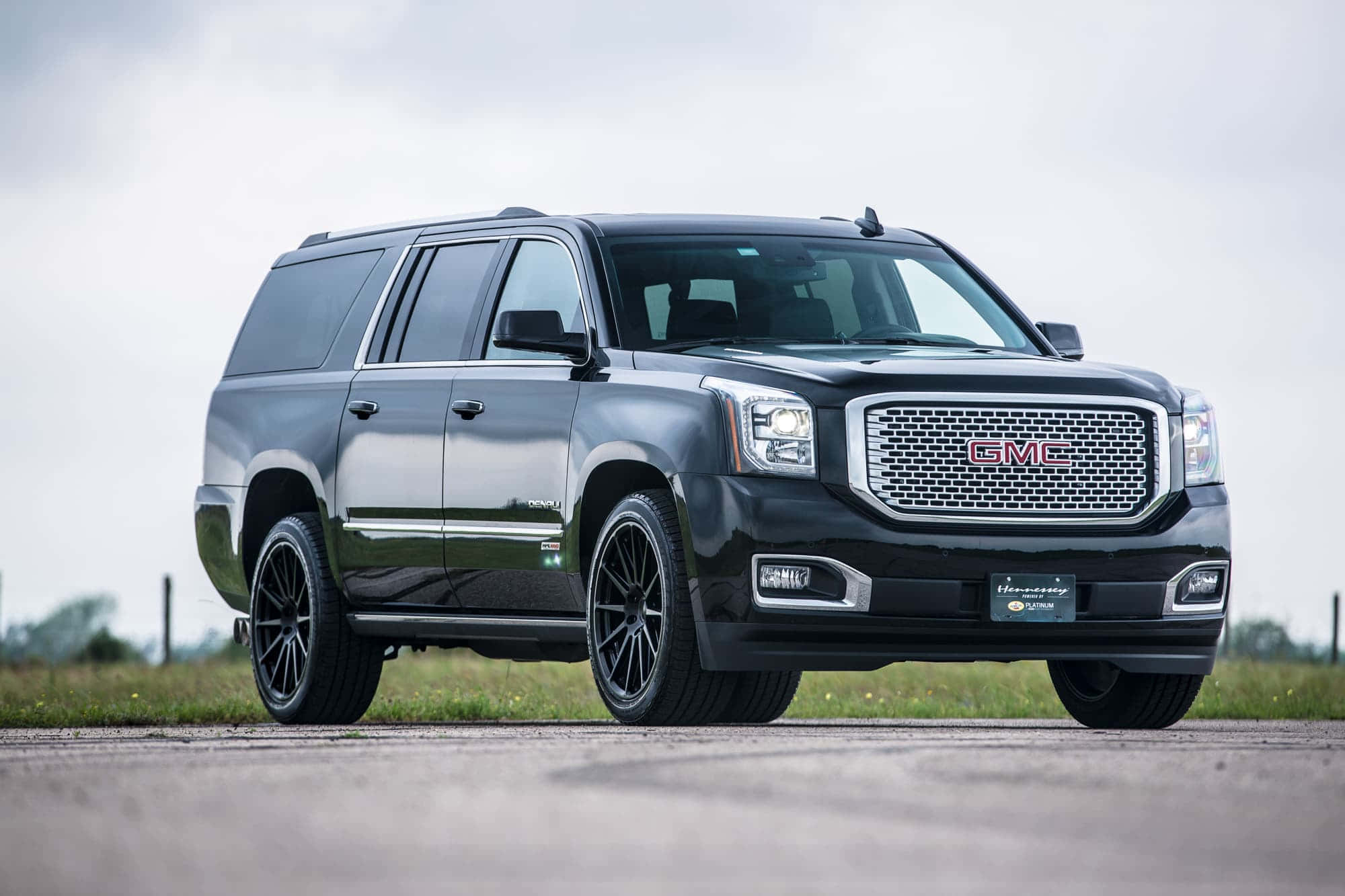 Gmc Yukon 桌布 壁紙 — 一輛時尚的黑色GMC Yukon XL SUV，配備定制黑色輪圈，停泊在鋪砌道路上，背景是陰天。