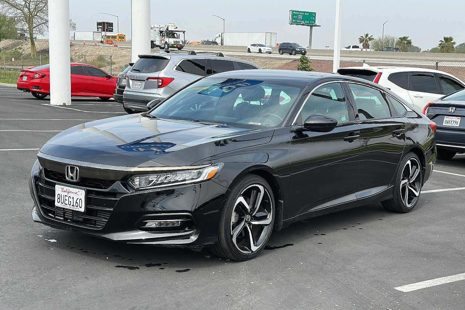 Honda Accord 桌布 壁紙 — 一輛時尚黑色本田雅閣房車停放在繁忙的瀝青停車場，背景有其他車輛和高速公路標誌。
