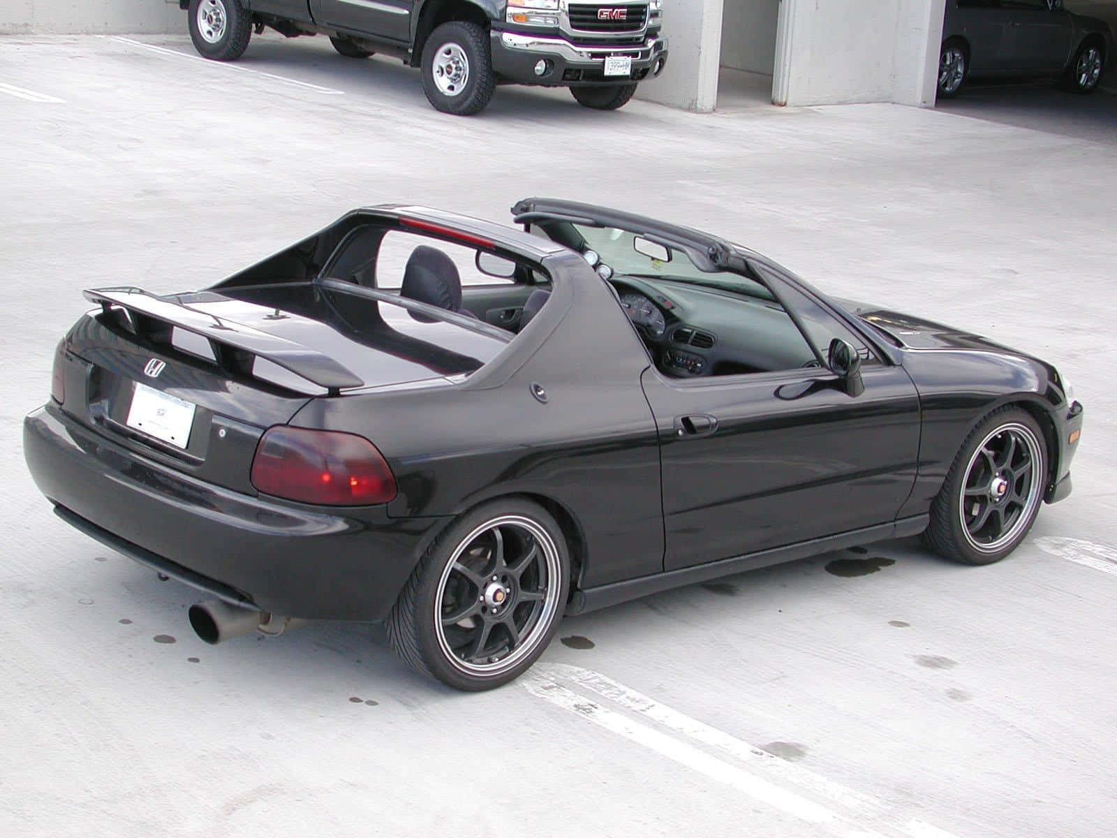 Honda Civic Del Sol 桌布 壁紙 — 一架時尚的黑色本田S2000敞篷跑車停放在混凝土停車場，背景有一輛GMC卡車。