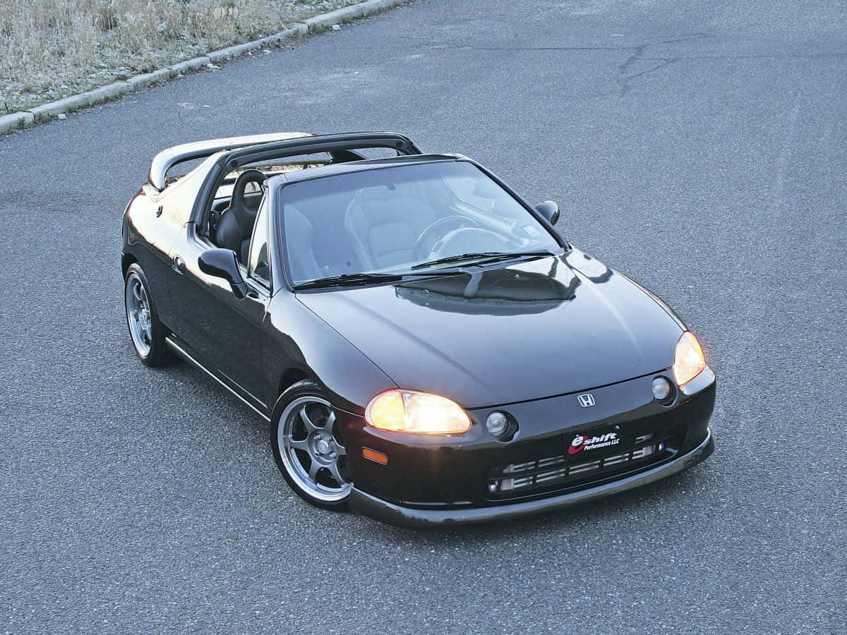 Honda Civic Del Sol 桌布 壁紙 — 一輛時尚的黑色本田S2000敞篷車，帶有發光頭燈，停在瀝青路上。