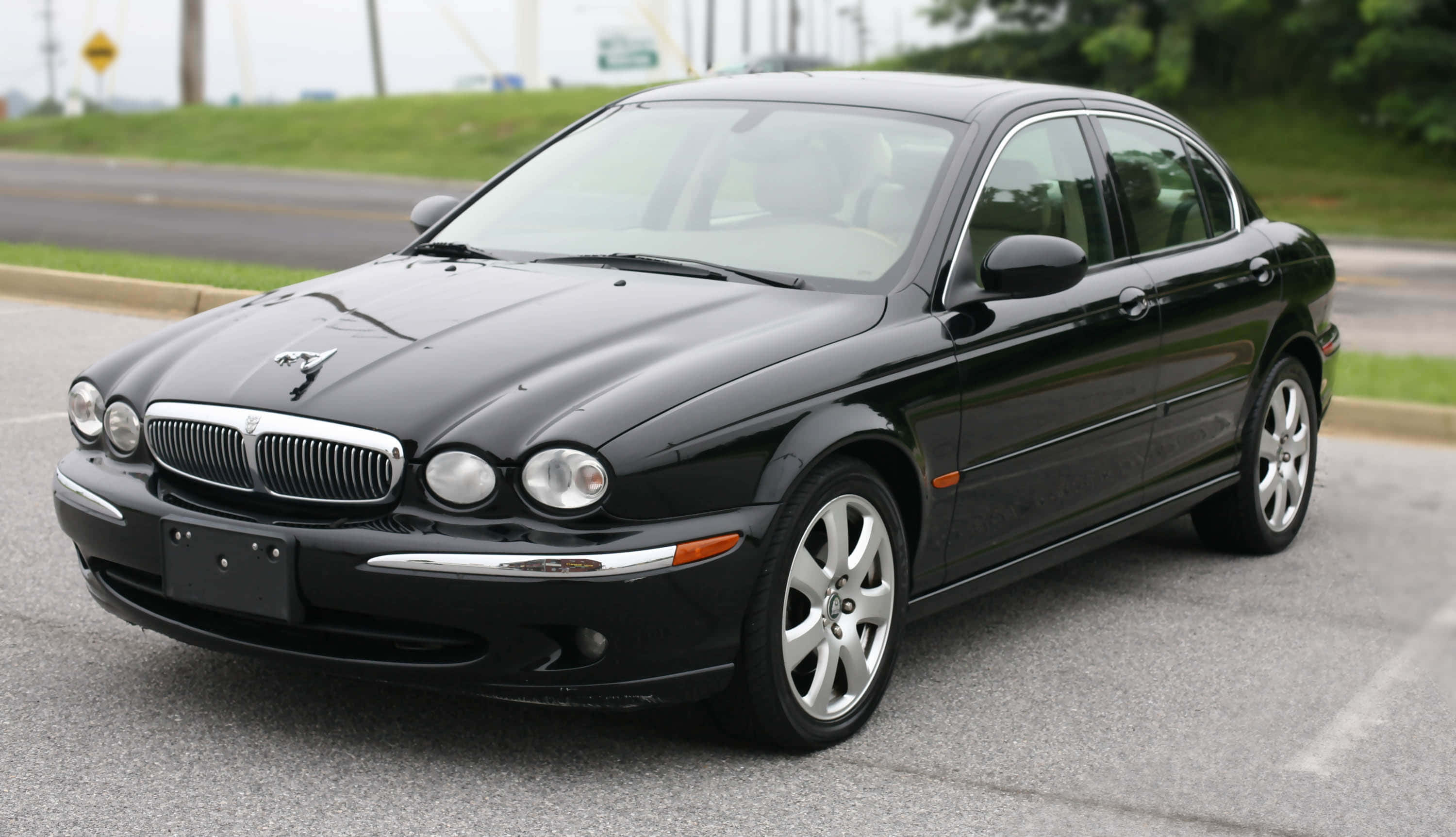 Jaguar X-type 桌布 壁紙 — 一輛時尚的黑色積架轎車停在柏油路上，背景有綠草和樹木。