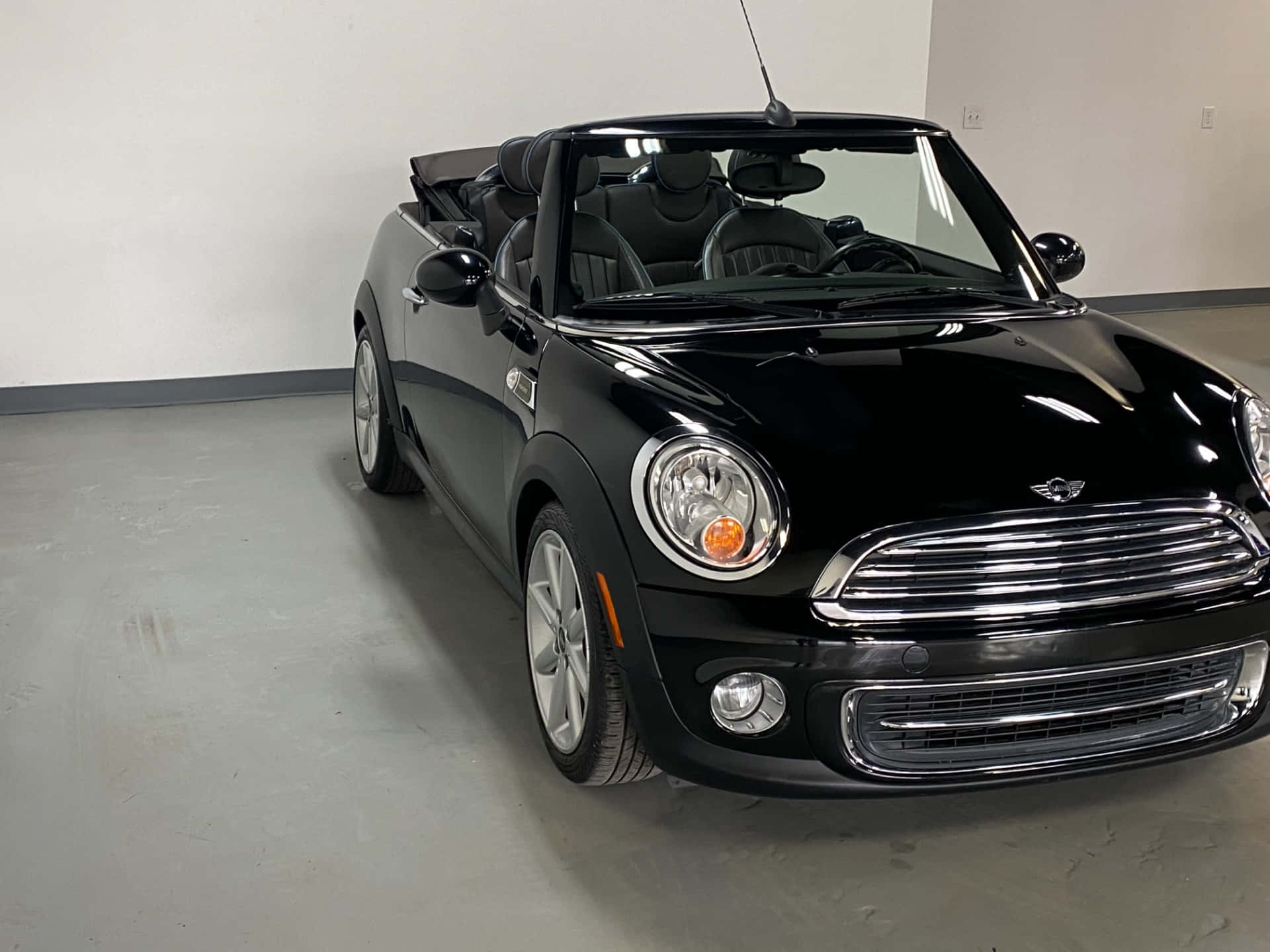 Mini Cooper Convertible 桌布 壁紙 — 一架時尚的黑色MINI Cooper敞篷車在室內停泊，車篷打開，光澤表面反射天花板燈光。