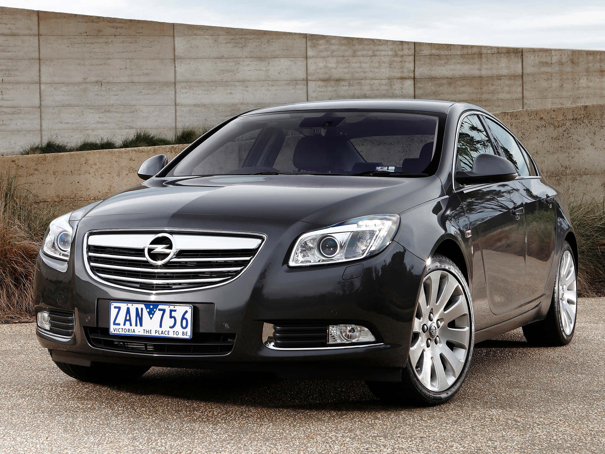 Opel Insignia 桌布 壁紙 — 一輛時尚的黑色歐寶Insignia轎車停在碎石上，背景有混凝土牆和乾草。