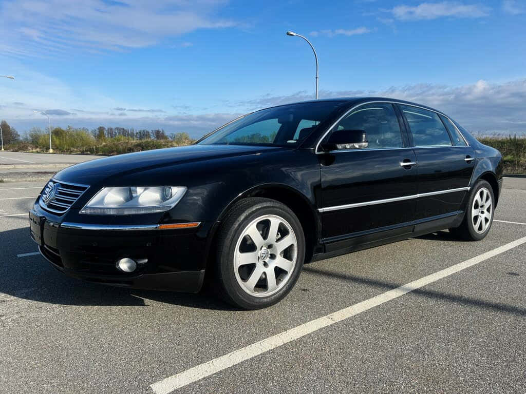Volkswagen Phaeton 桌布 壁紙 — 一輛時尚的黑色福斯Phaeton轎車停放在陽光普照的瀝青停車場，天空湛藍，白雲點綴。