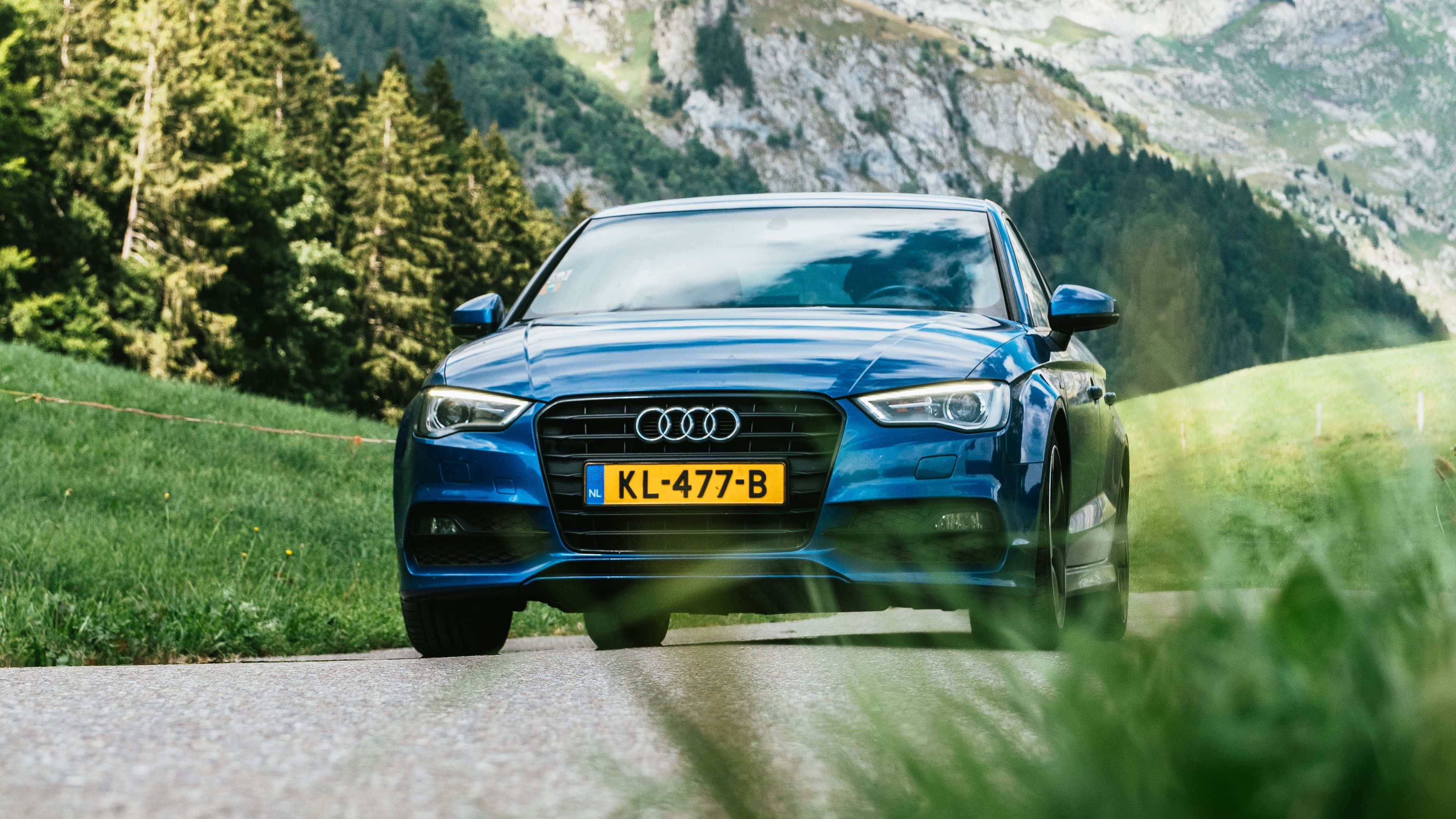 Audi Q7 桌布 壁紙 — 一輛時尚的藍色奧迪轎車沿著蜿蜒的山路行駛，周圍是茂密的綠色森林和岩石山峰。