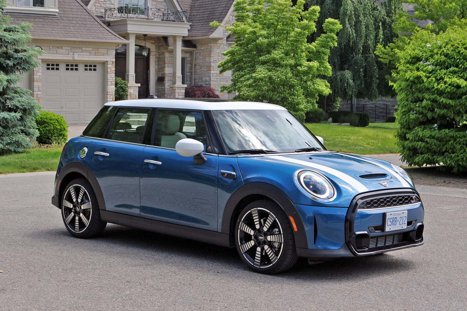 Mini Cooper S 桌布 壁紙 — 一架時尚的藍色電動MINI Cooper停放在郊區車道上，旁邊是石屋和茂密的綠樹。